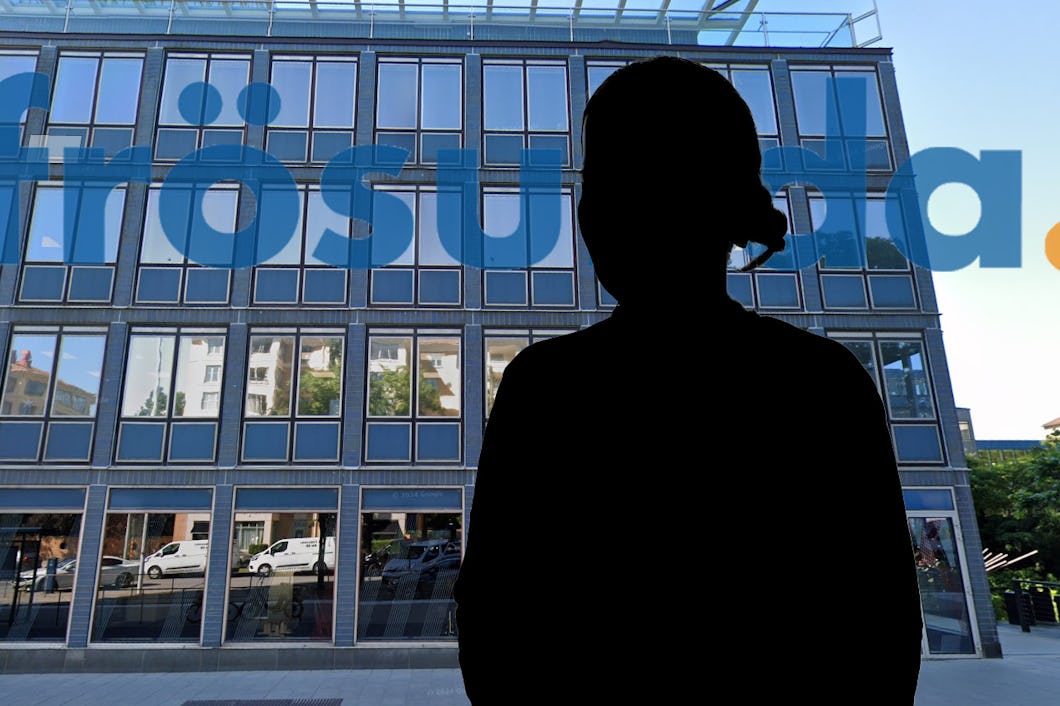 En silhuett av en person står framför en modern byggnad med glasfasad. Bilar och träd reflekteras i fönstren.