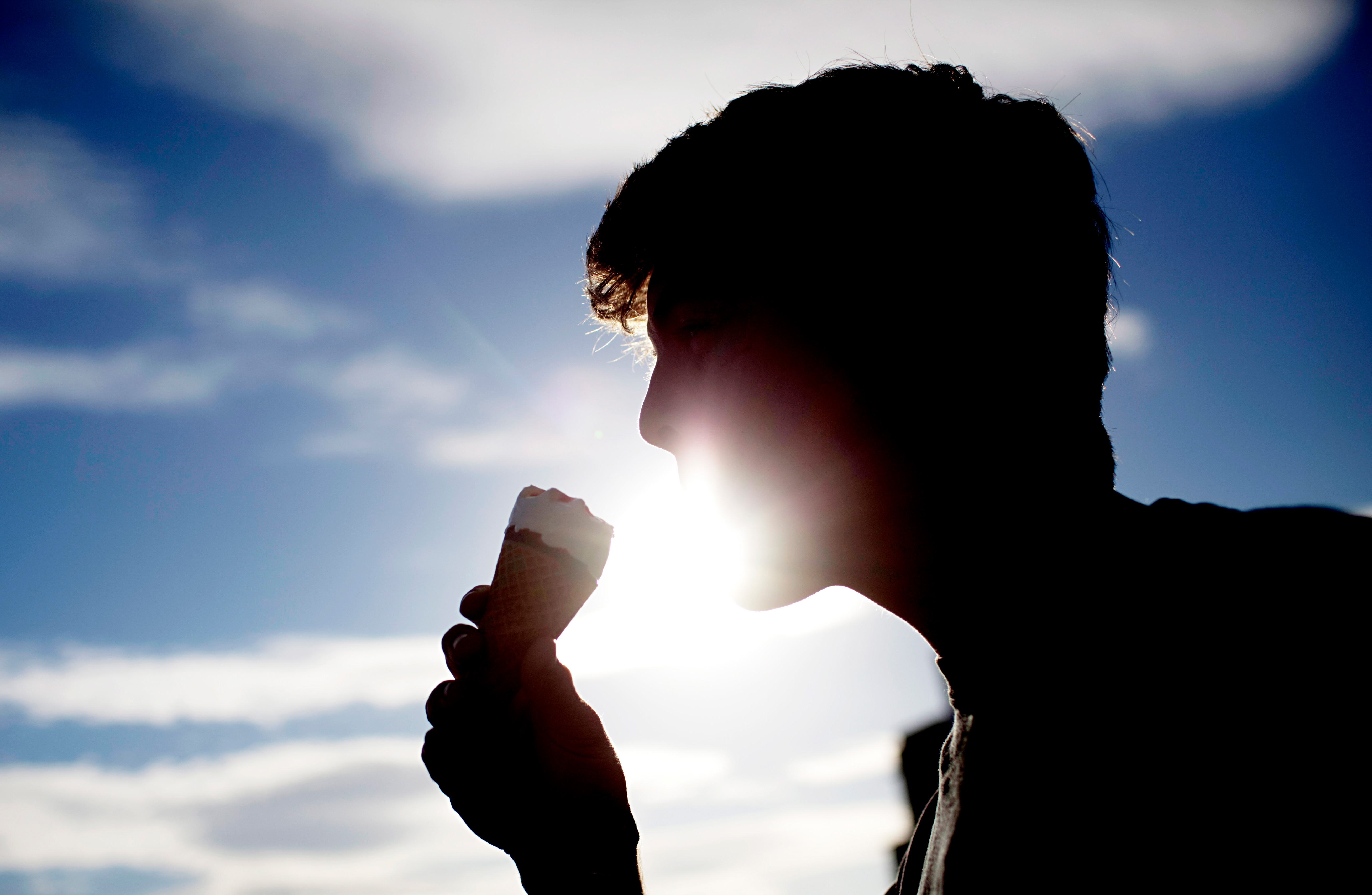 En siluett av en person som äter en glasstrut med himlen som bakgrund.