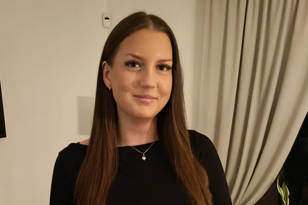 En person med långt brunt hår och en svart topp står inomhus.