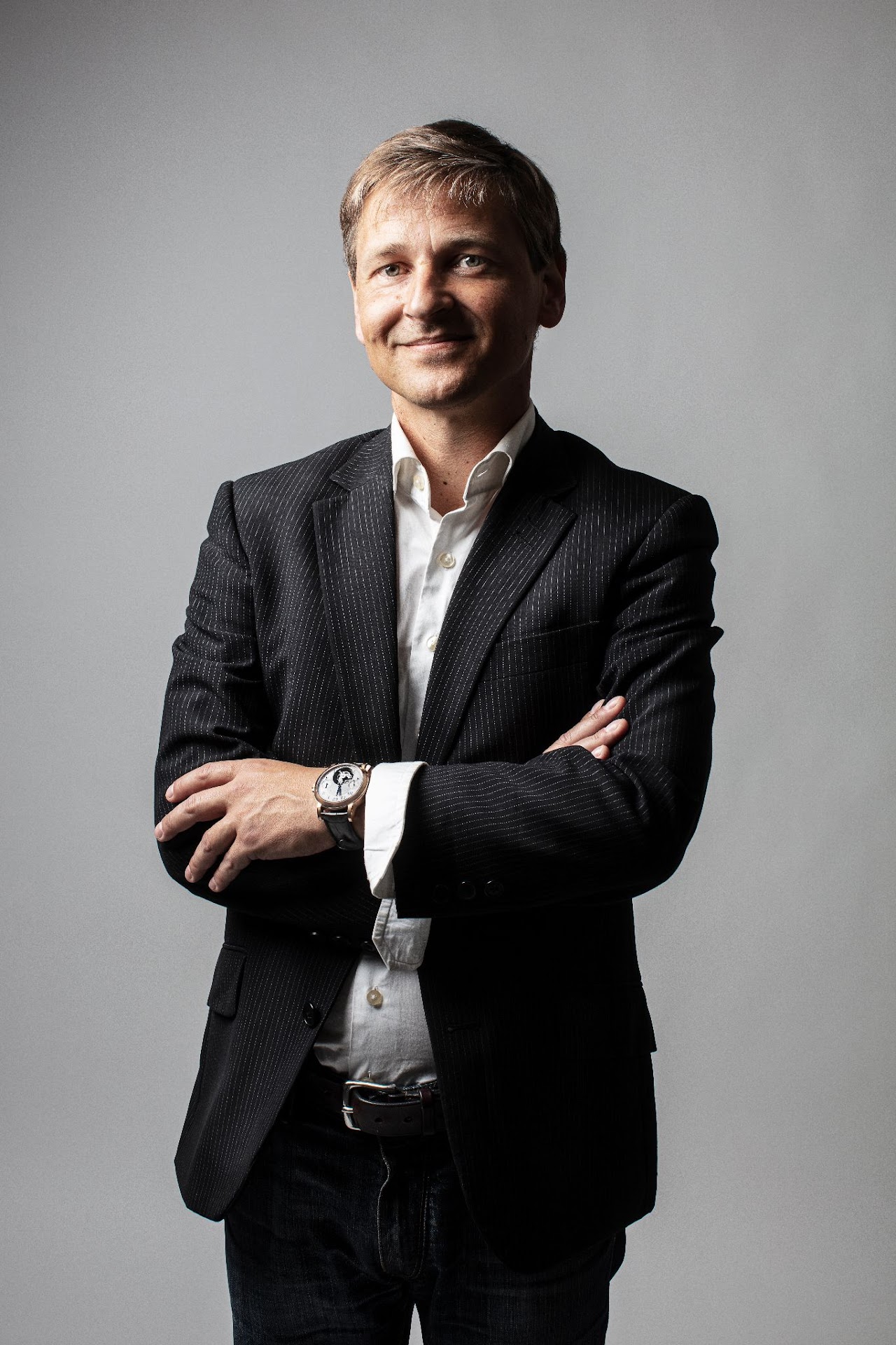 Petri Kajonius står med armarna korsade framför en enfärgad grå bakgrund, med ett leende på läpparna.