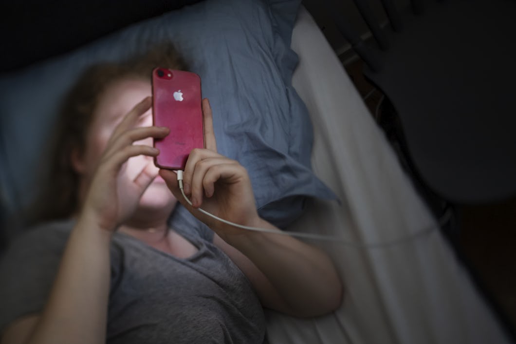 Person ligger i sängen och använder en röd smartphone med ansluten laddningskabel.