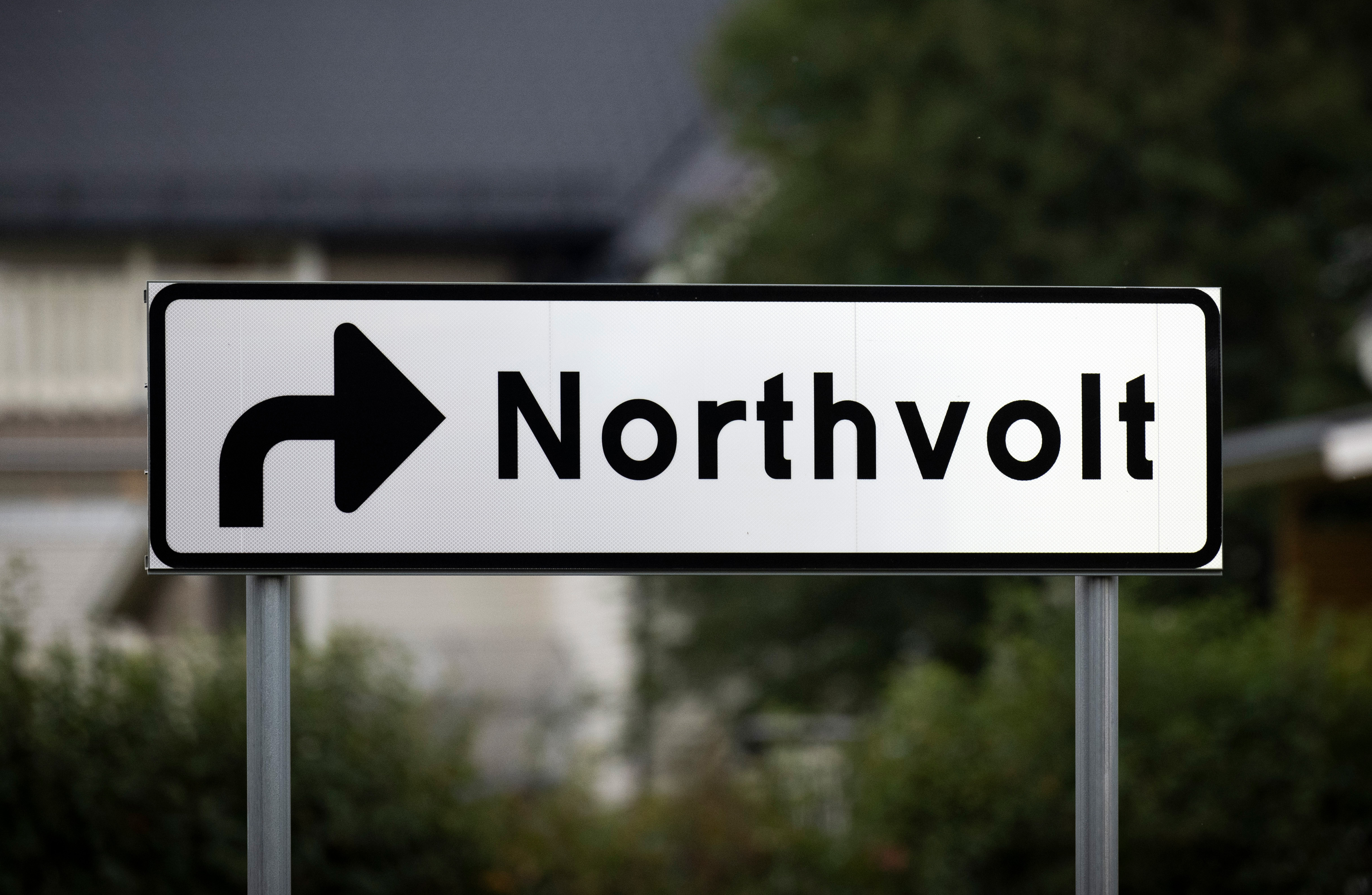 Skylt med en pil som pekar åt höger och har texten "Northvolt", mot en suddig bakgrund av grönska och en byggnad.