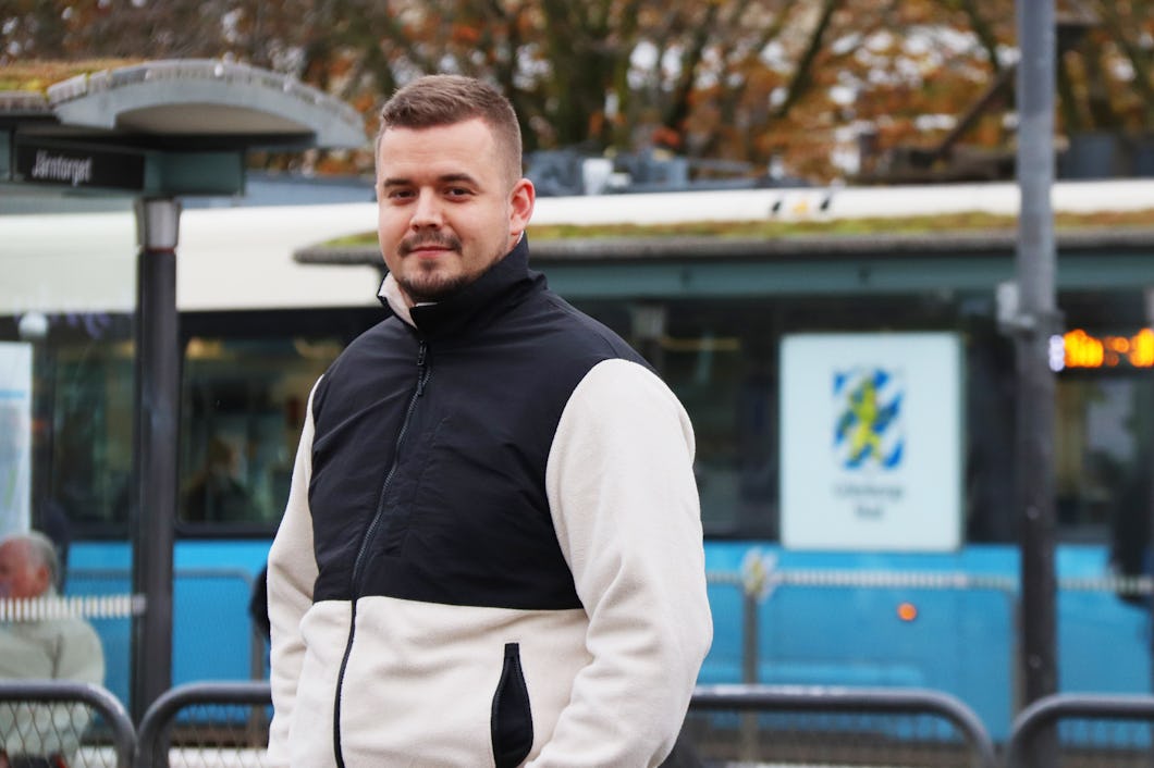En man står vid en spårvagnshållplats och har på sig en svartvit jacka.