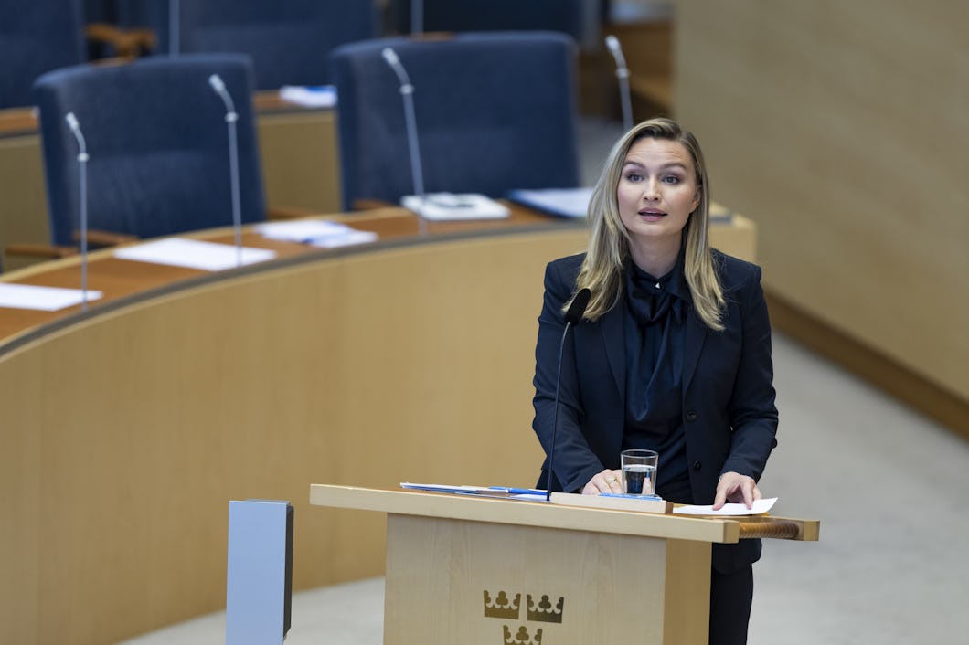 Ebba Busch talar vid ett podium i Riksdagens plenisal.