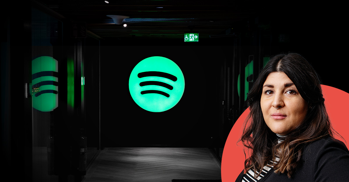 En kvinna står bredvid en stor upplyst grön Spotify-logotyp i ett mörkt rum.