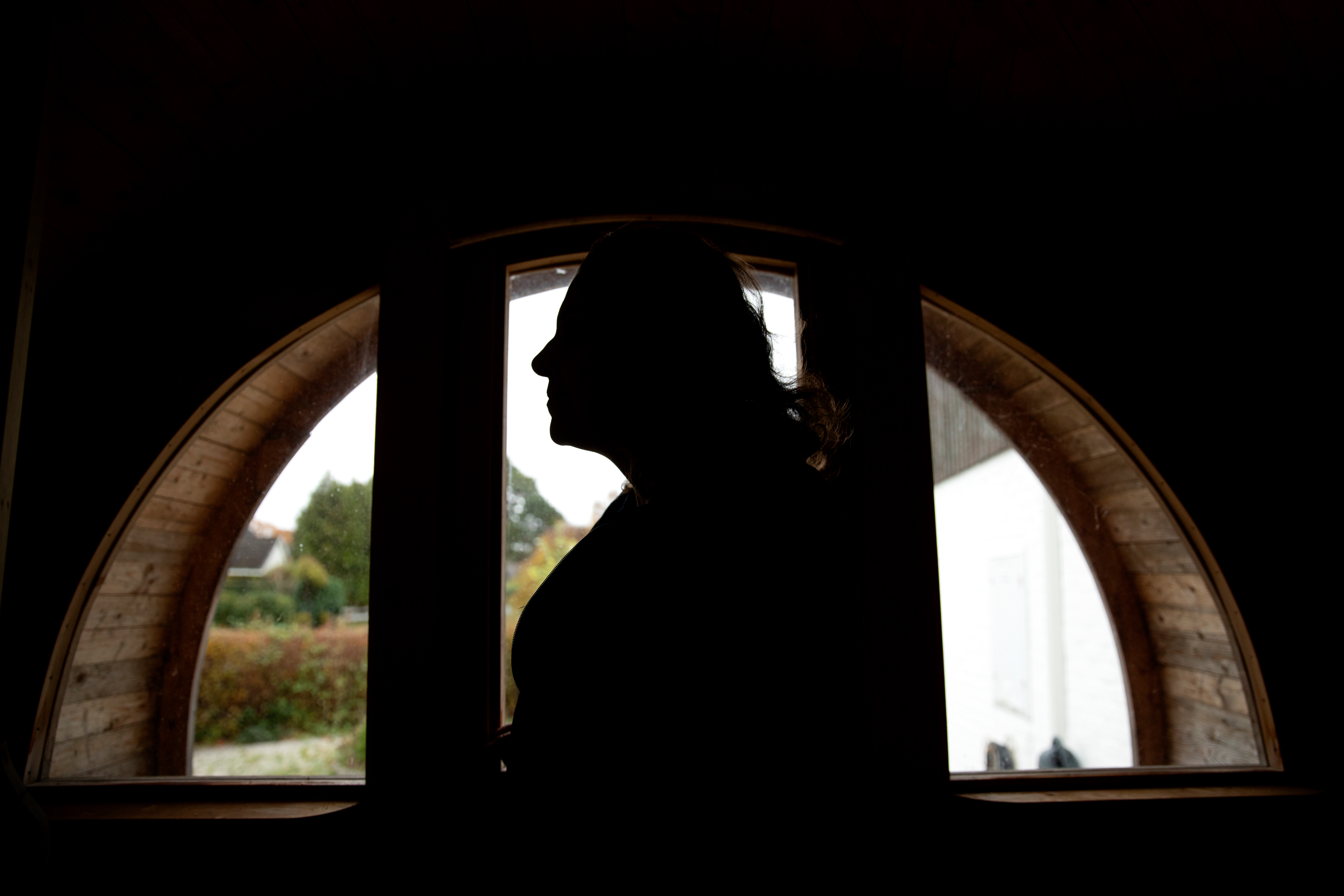 En silhuett av en person står framför ett bågformat fönster med svagt synlig utsikt utanför.