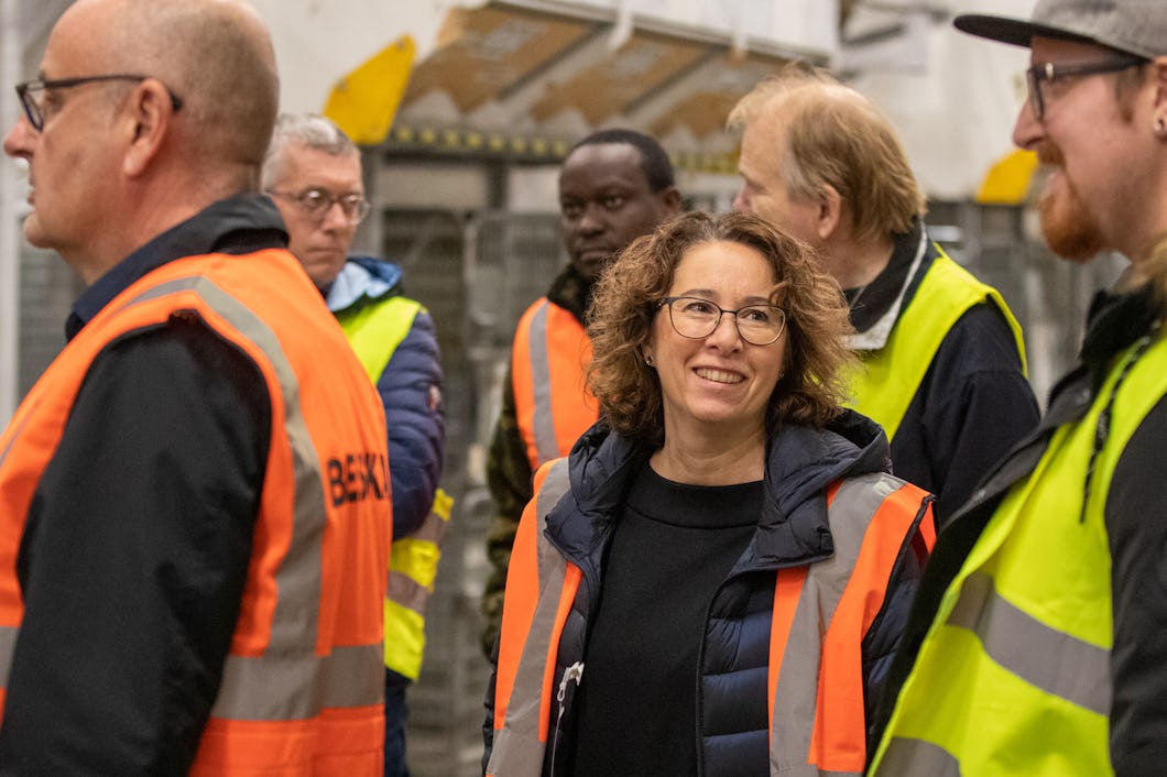 En grupp människor iförda säkerhetsvästar står och samtalar i en industriell miljö.