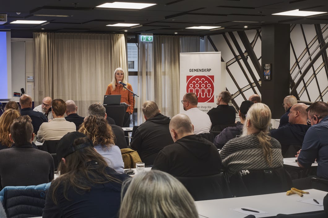 Eva Guovelin talar vid ett podium framför en publik i ett konferensrum.