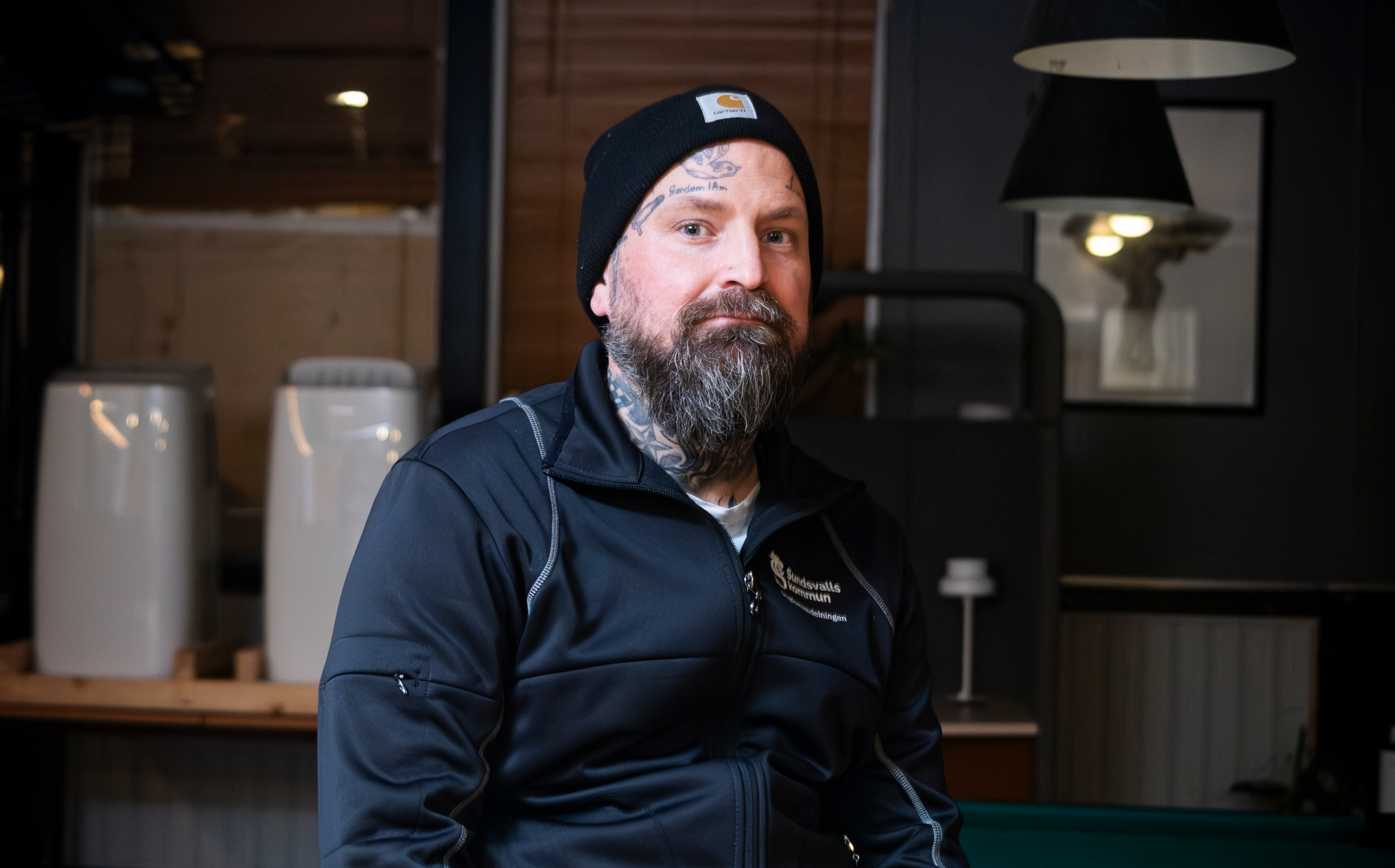 Stefan Fernaeus med tatueringar och skägg bär en svart mössa och jacka. Han sitter inomhus och tittar mot kameran.