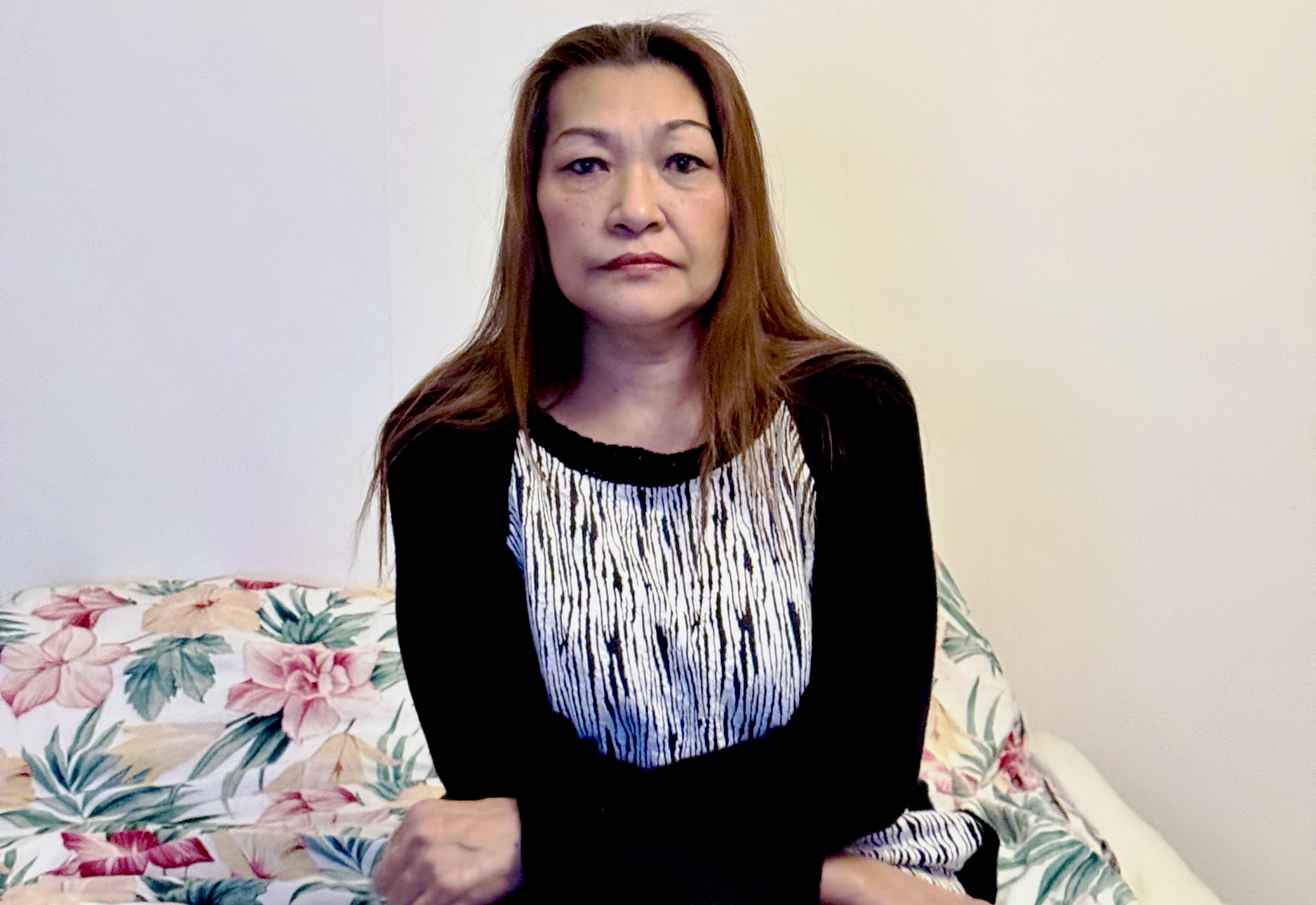 Nittaya Jampeesri med långt hår sitter på en säng med blommigt mönstrade sängkläder och har på sig en svartvit tröja. Bakom dem syns en enfärgad vägg.