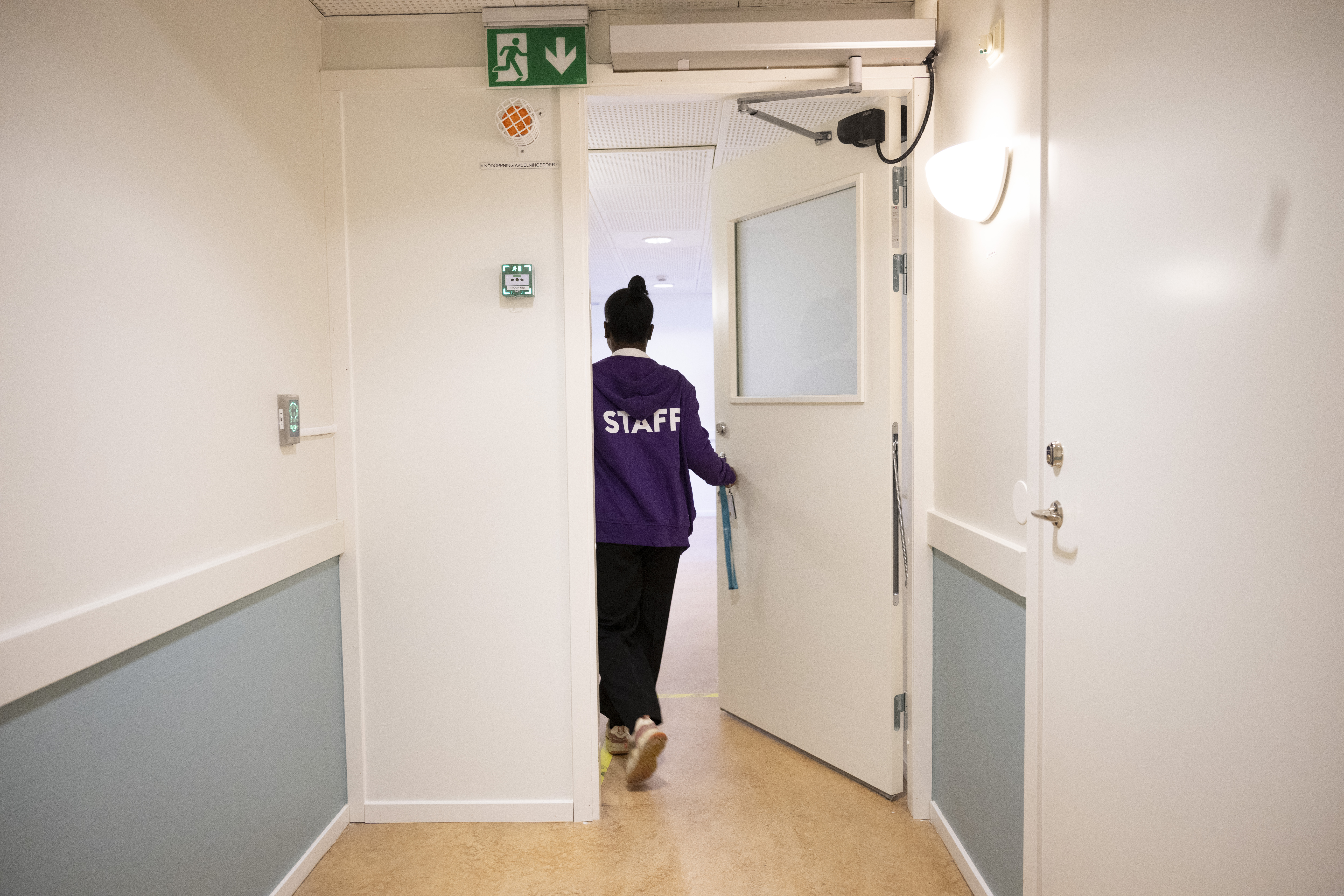 En person med en lila jacka märkt "Staff" går genom en dörröppning i en korridor i en byggnad.