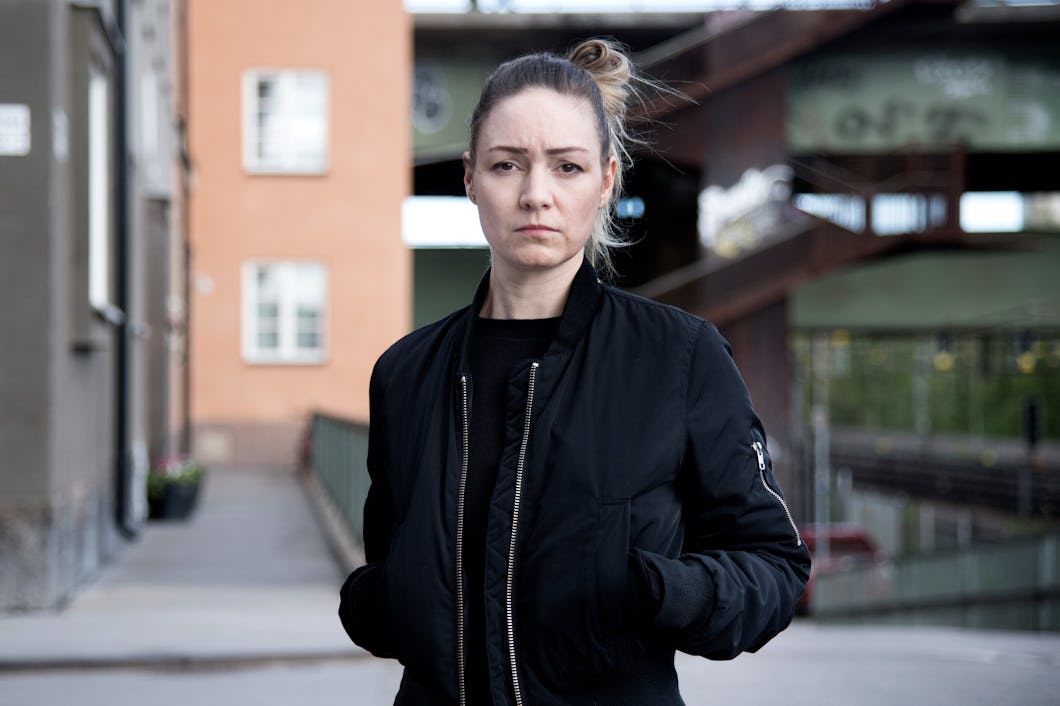 Kvinna som står utomhus och har på sig en svart jacka. I bakgrunden syns byggnader och en viadukt.