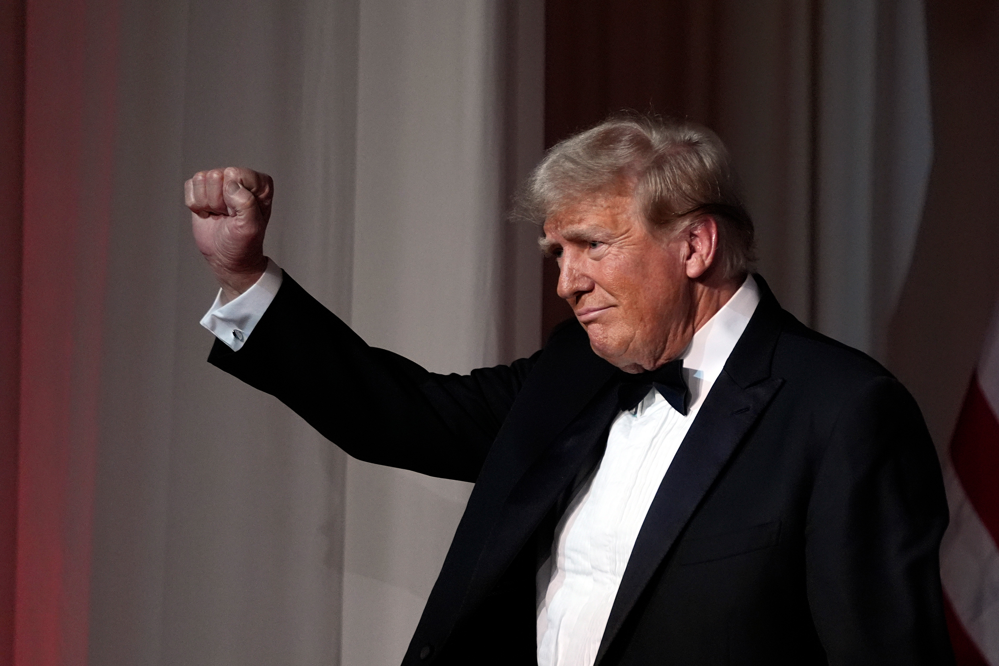 En man i smoking höjer sin knutna näve i luften vid ett inomhusevenemang.