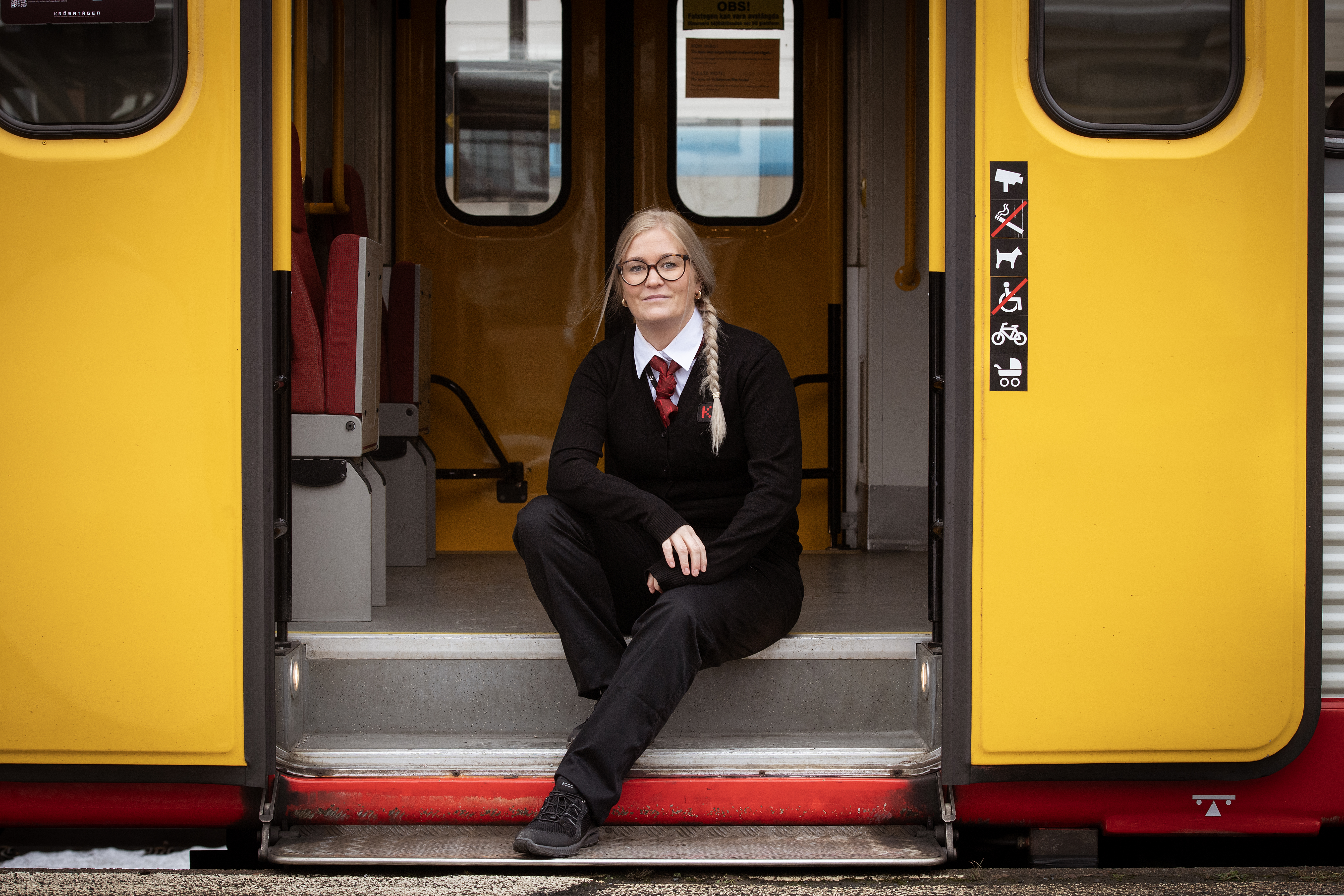 Emelie Lundborg i uniform sitter på trappsteget till ett gult Krösatåg.