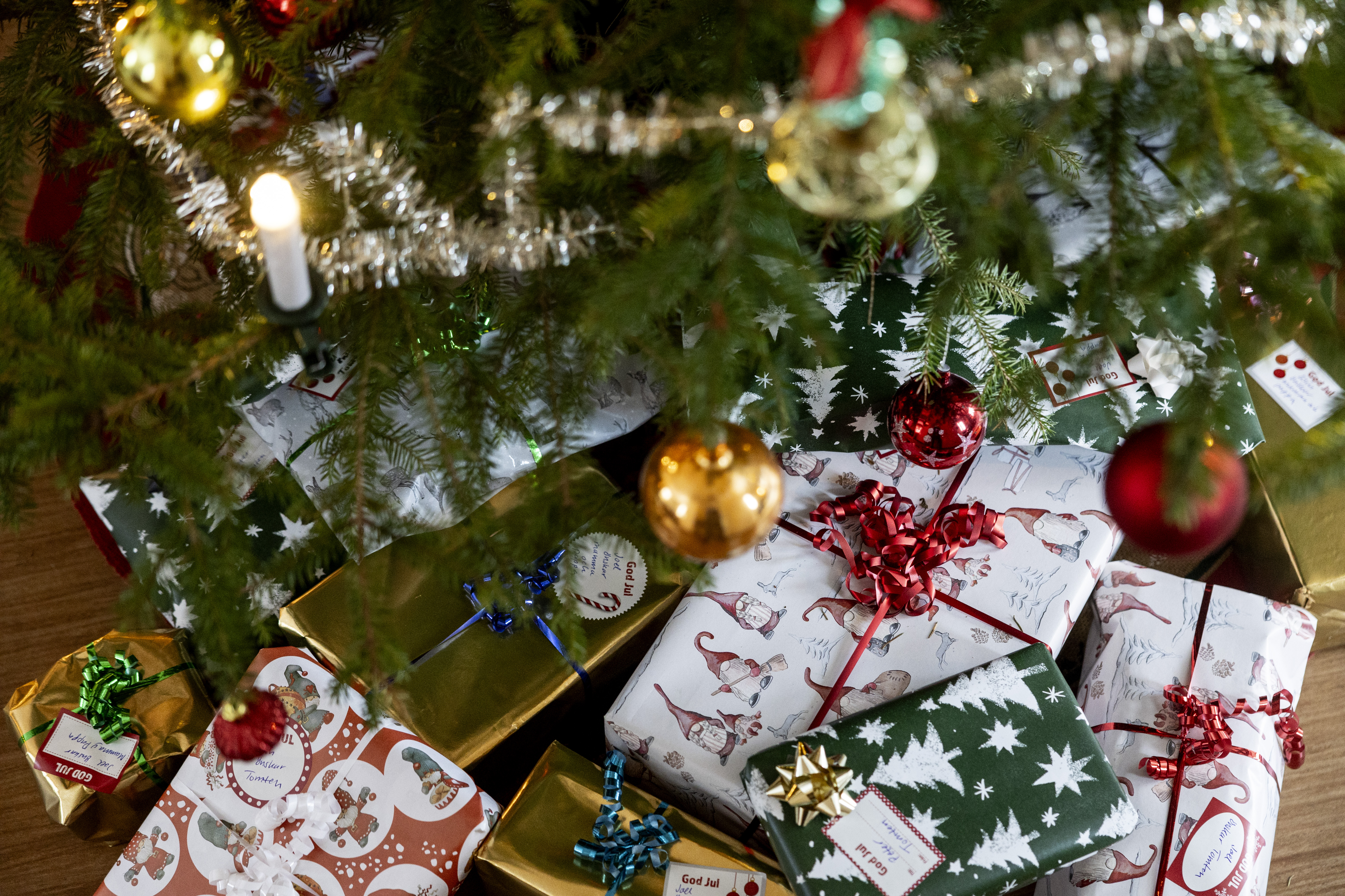 Flera inslagna paket ligger under en julgran med prydnader, glitter och ett ljus.