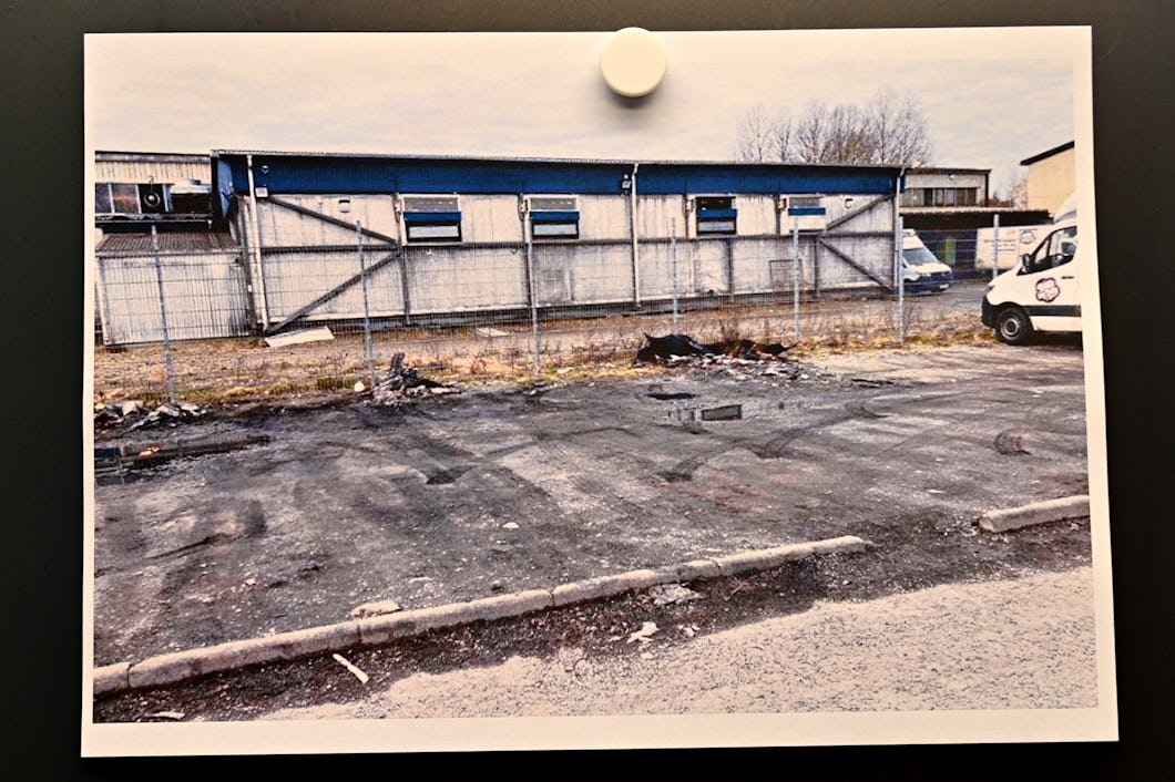 Bild av en parkeringsplats framför en låg industribyggnad där det ligger brända föremål på asfalten.