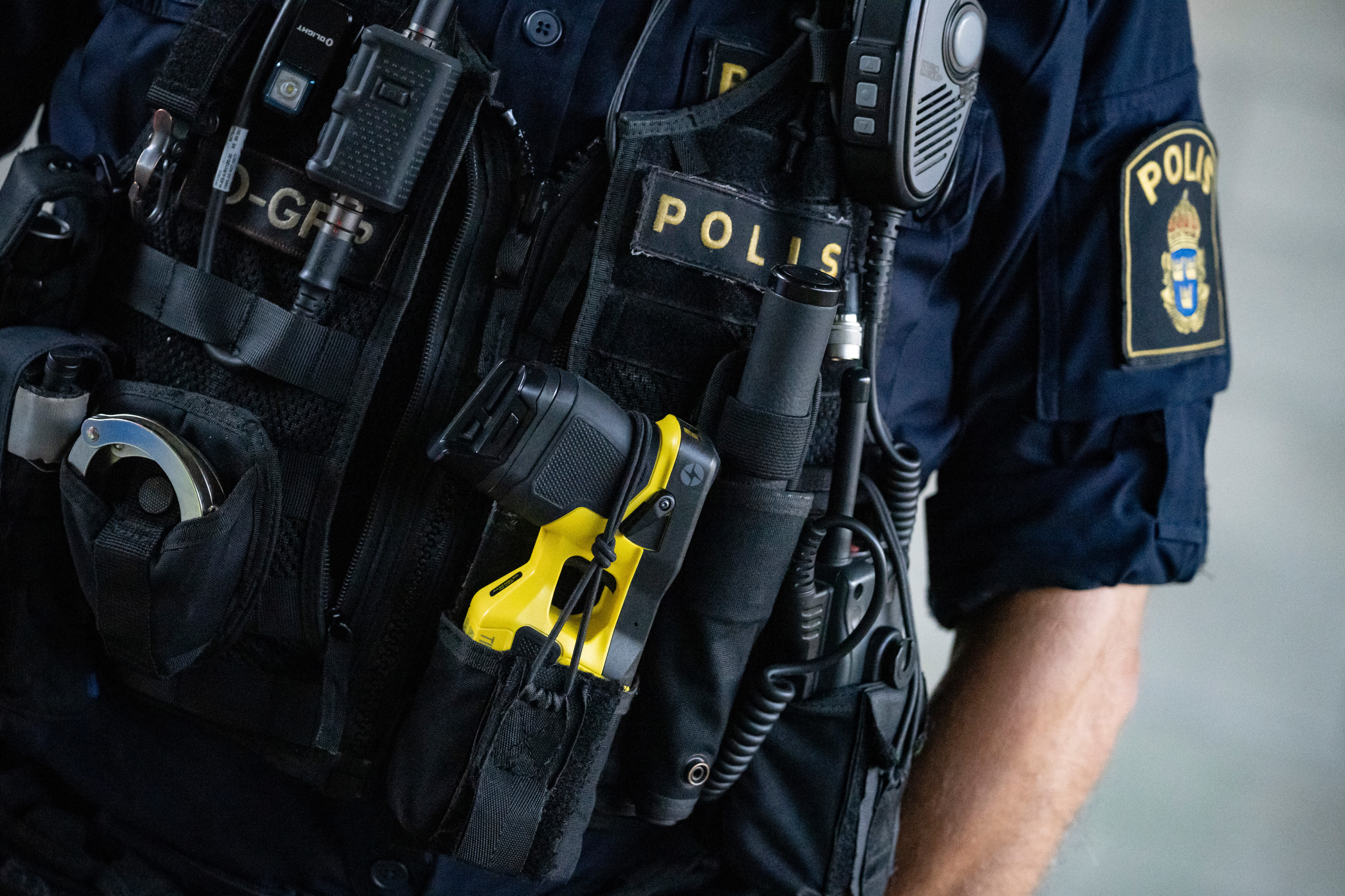 En polis i uniform bärande en radio och en gul elpistol på en taktisk väst.