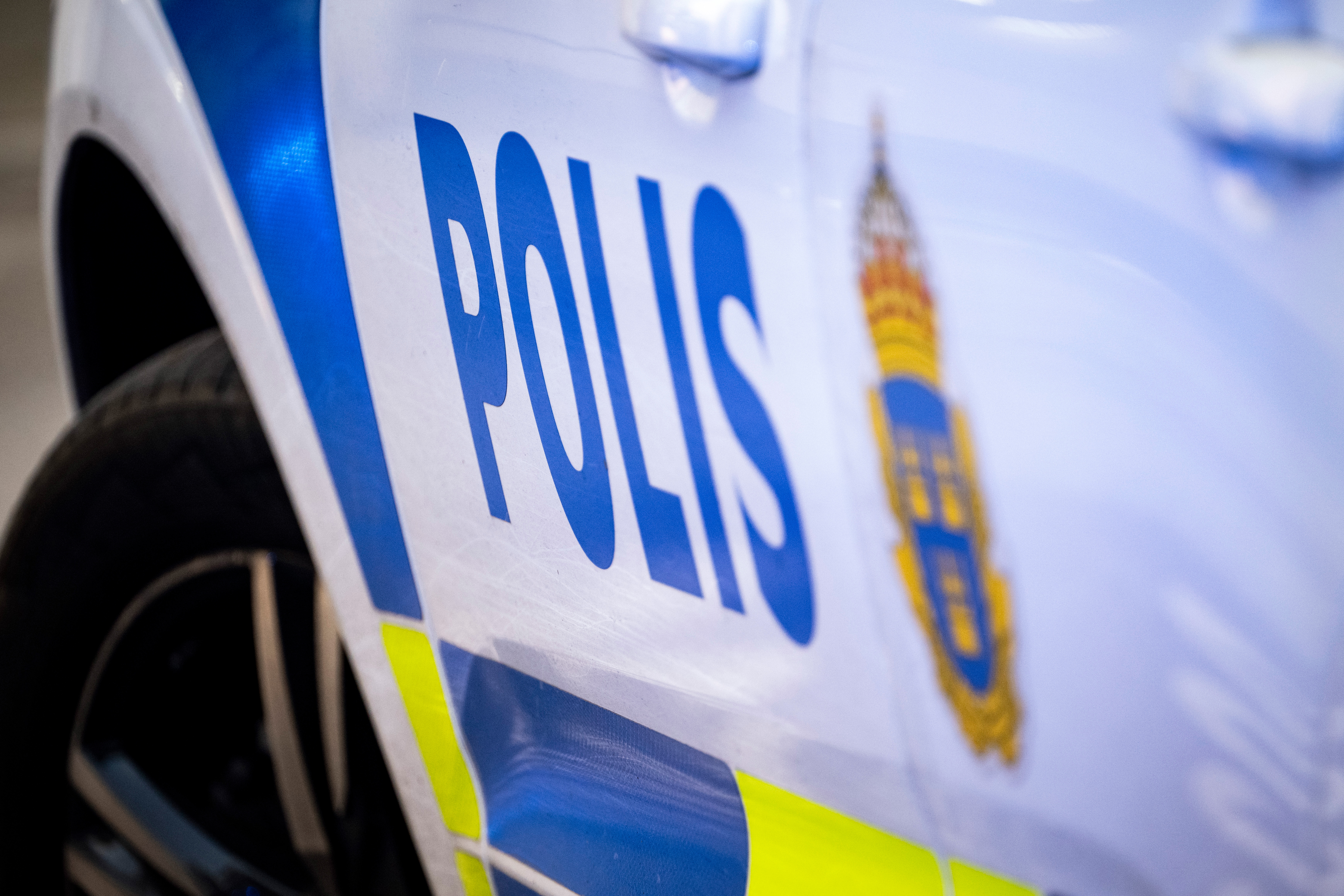 Sidan av ett svenskt polisfordon med ordet "Polis" och en del av Sveriges statsvapen synligt.