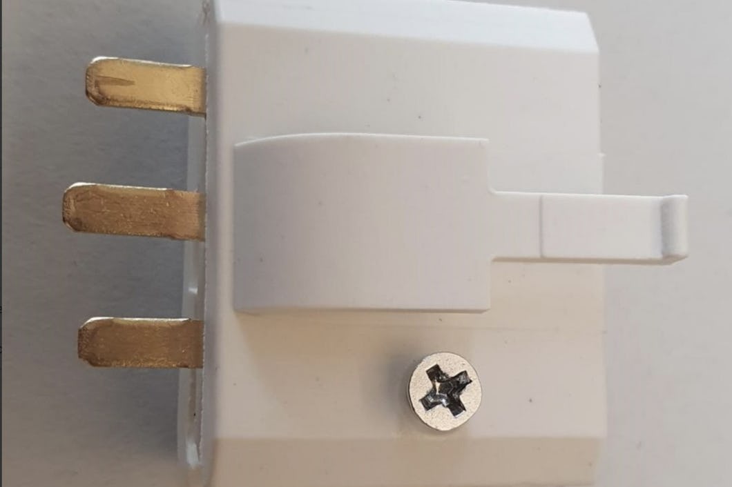 Bild av en vit eladapter med tre mässingskontakter och en skruv, placerad mot en enfärgad bakgrund.