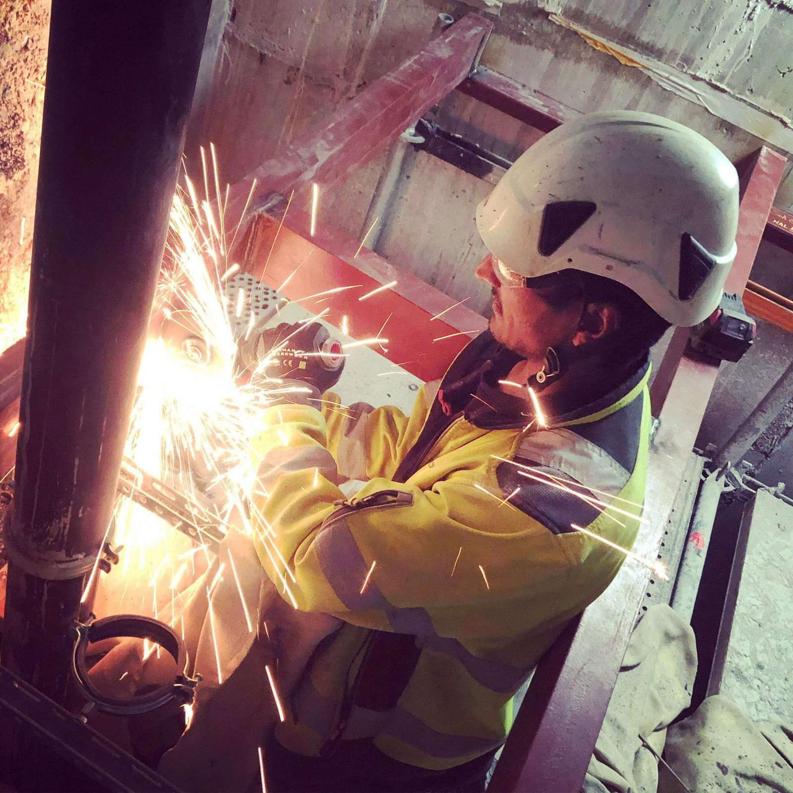 En arbetare i skyddsutrustning svetsar ett metallrör, vilket ingår i att gnistor flyger omkring i en industriell miljö.