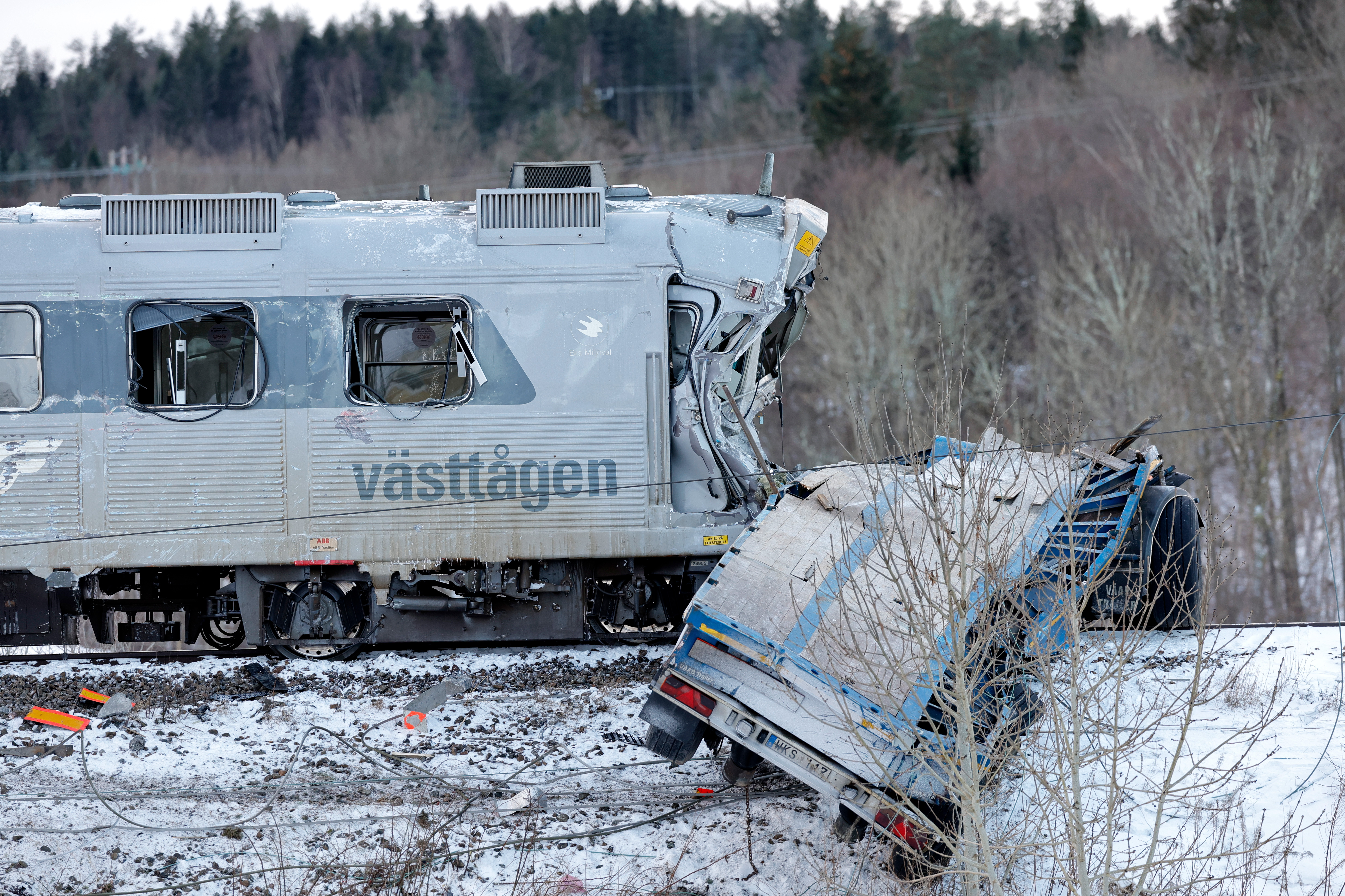 En trasig tåg med texten "Västtågen" och en delvis förstörd bil på ett snötäckt spår, med träd i bakgrunden.