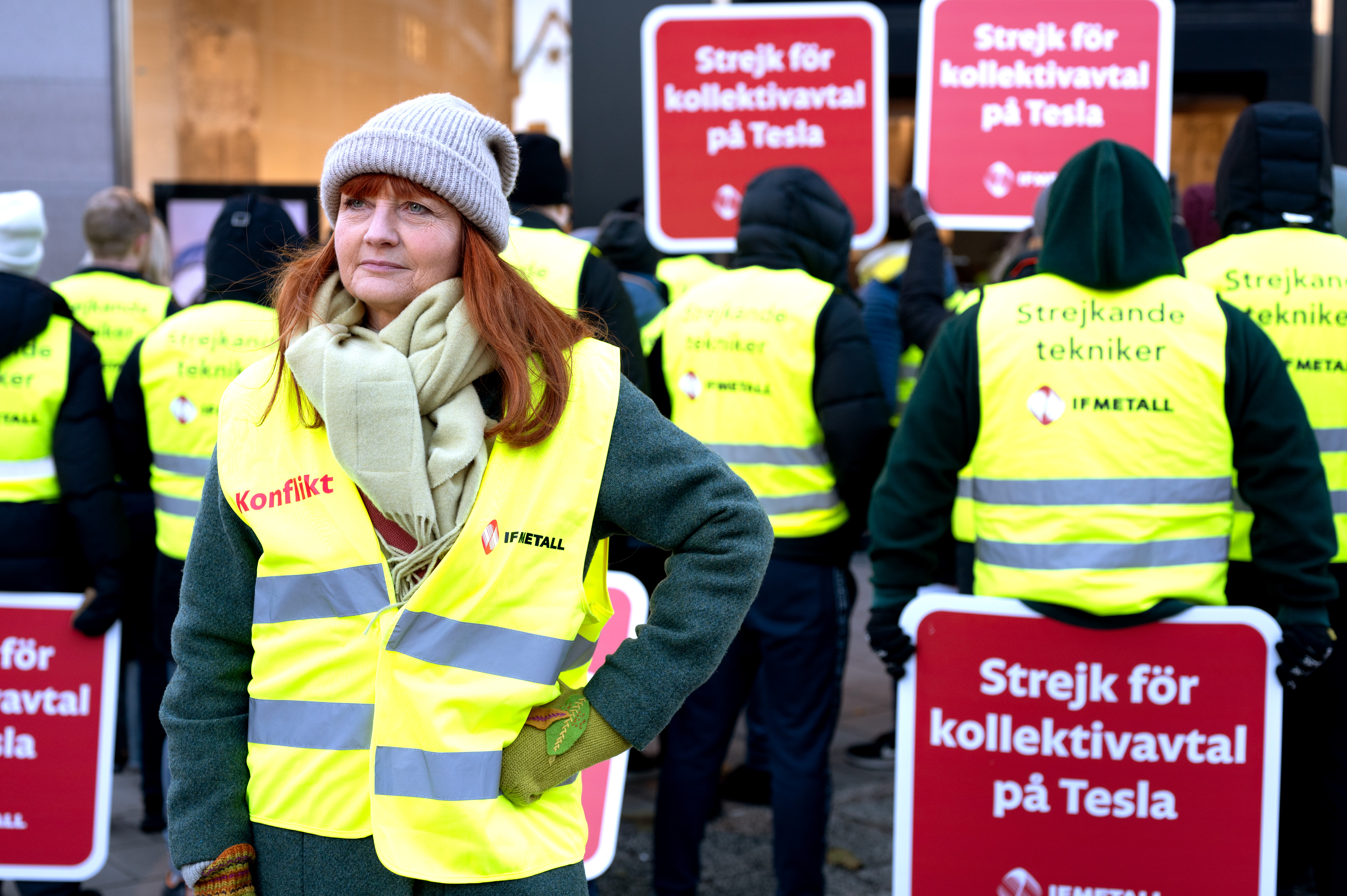 En grupp personer iförda gula västar håller upp skyltar med texten "Strejk för kollektivavtal på Tesla" under en demonstration. En kvinna står vänd mot kameran i förgrunden.