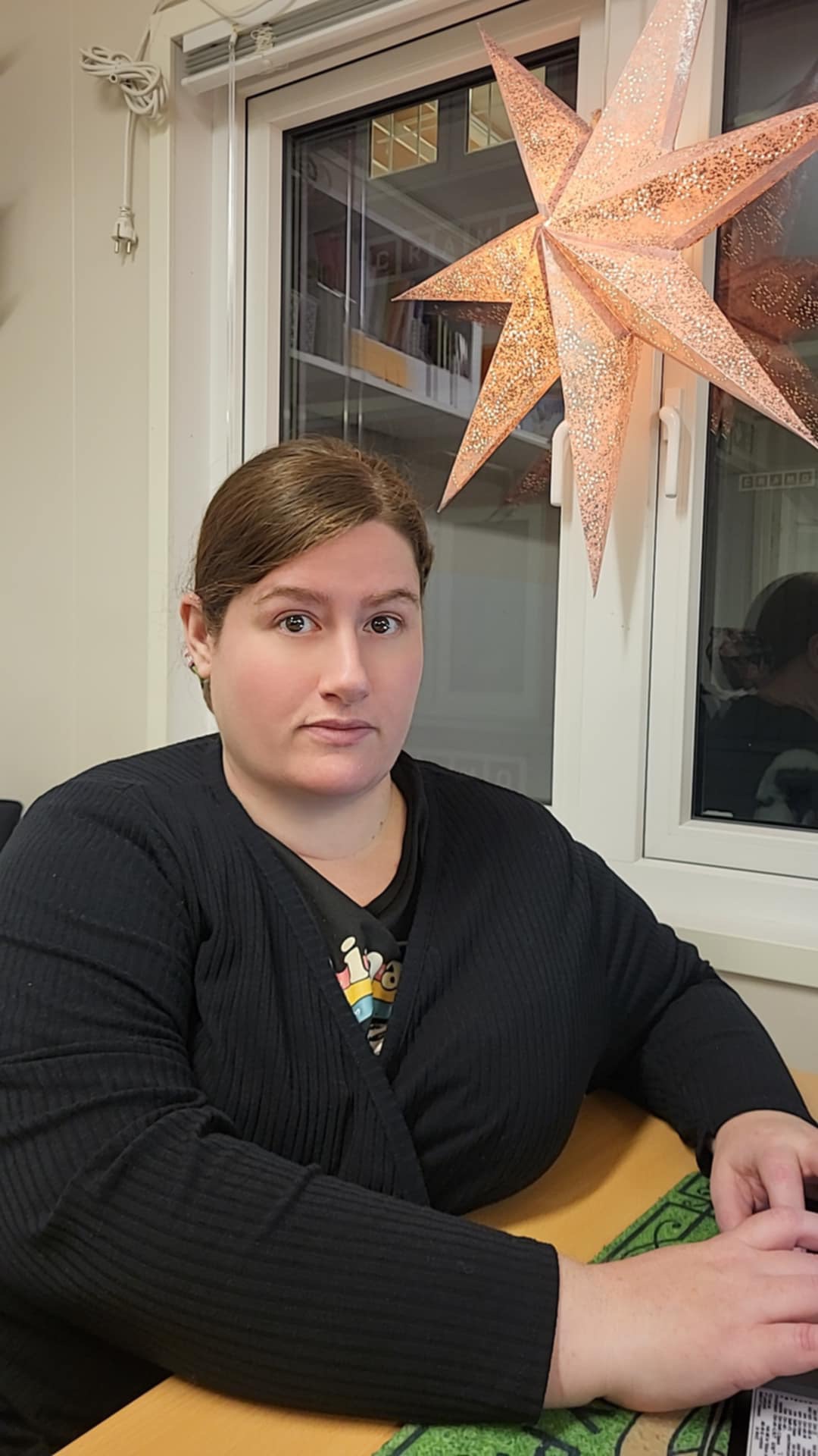 En person sitter vid ett bord nära ett fönster, och en stjärnformad lampa hänger ovanför.