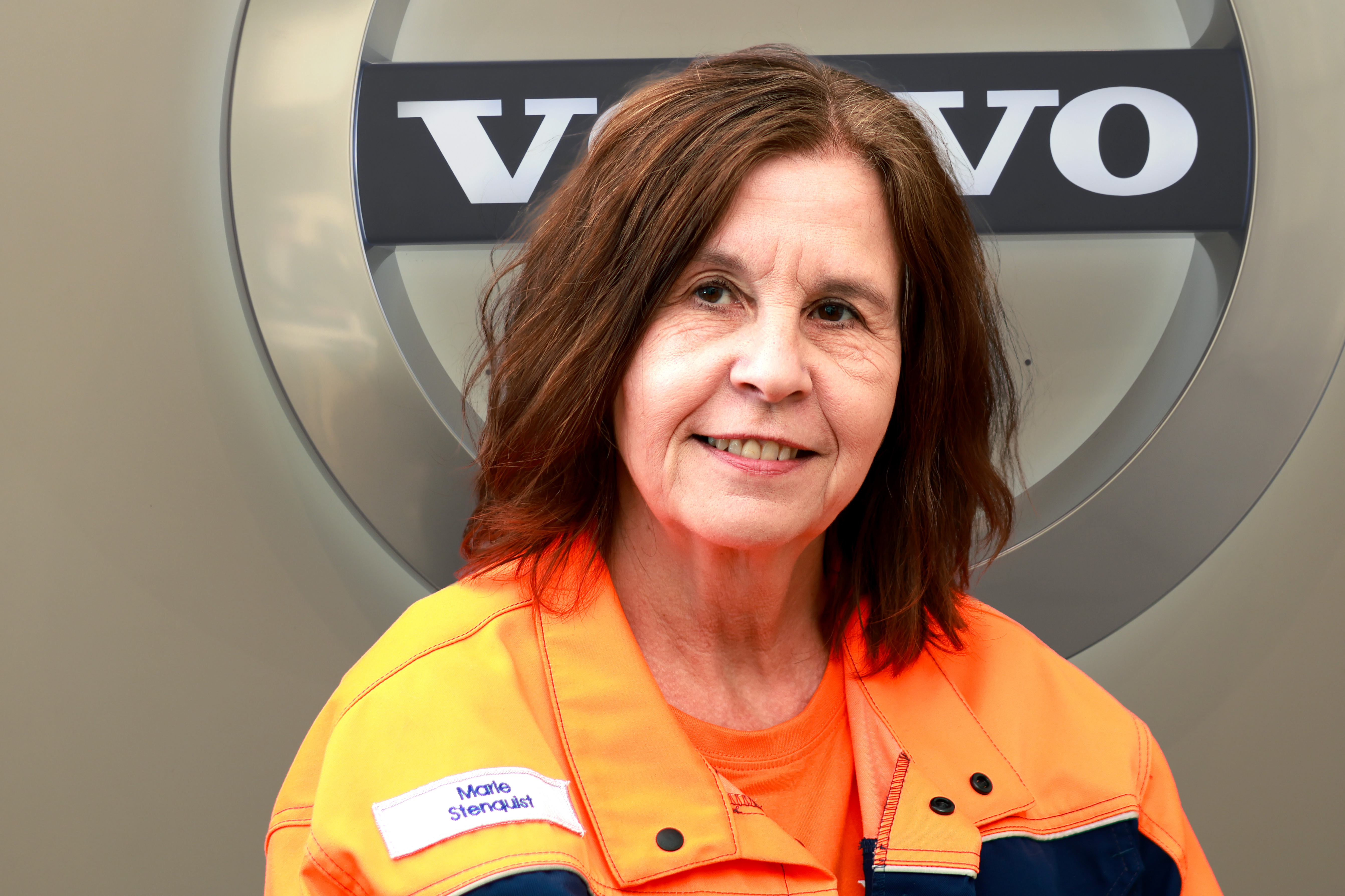 En person i orange jacka med namnbricka står framför en Volvo-logotyp.