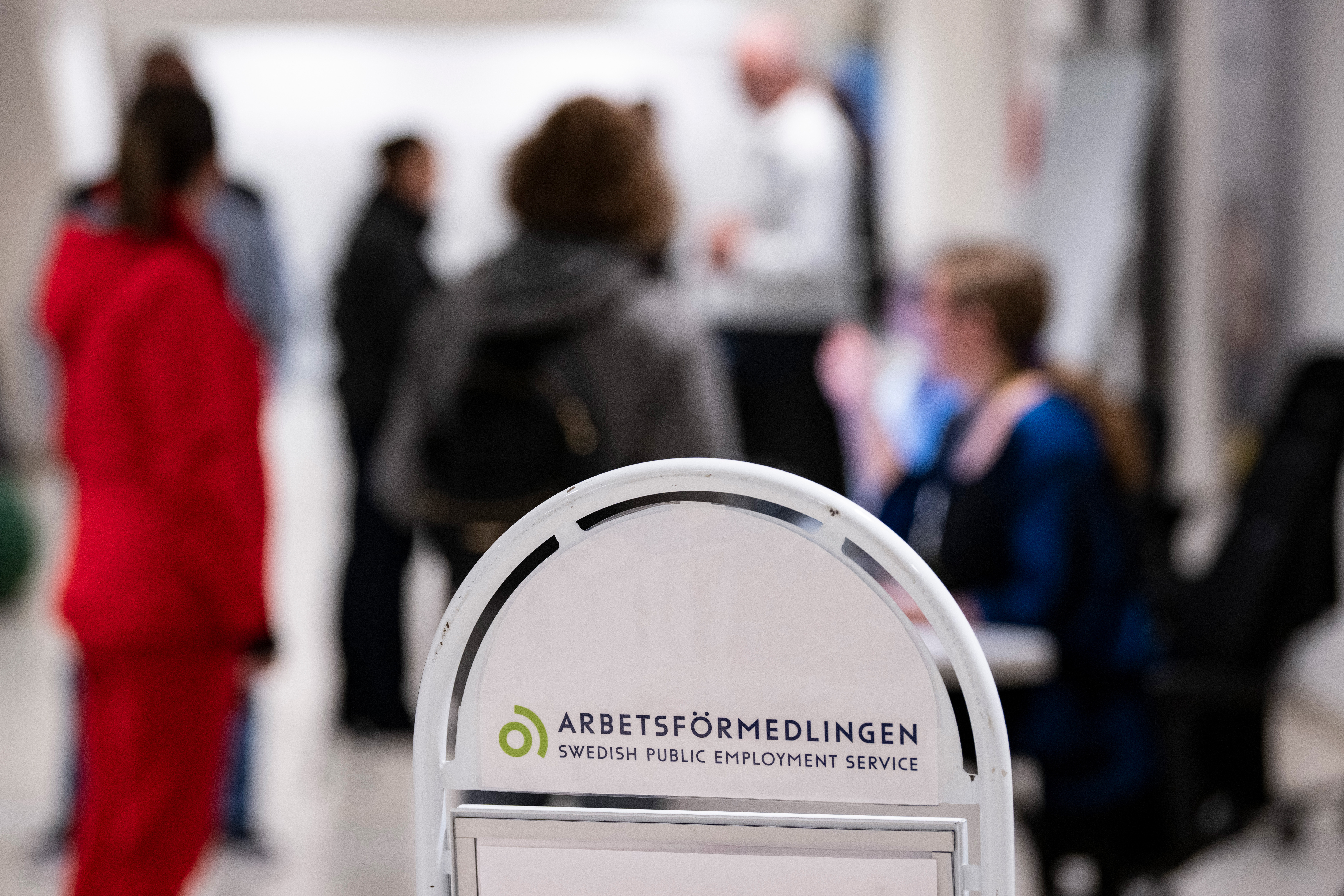 Skylt för "Arbetsförmedlingen" i fokus med suddiga personer i bakgrunden.