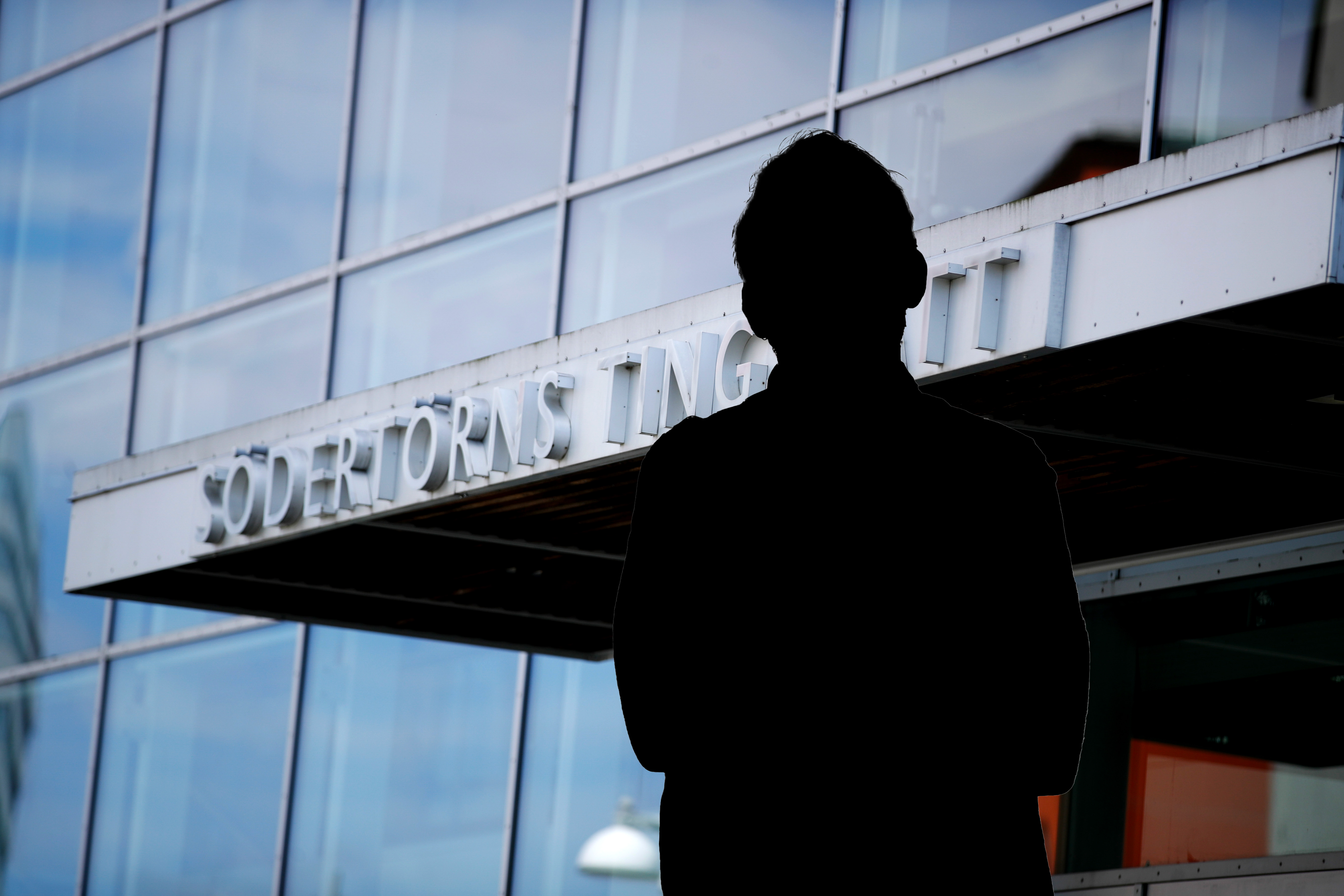 En person i silhuett står framför en byggnad med glasfönster och en skylt med texten "Södertörns Högskola".