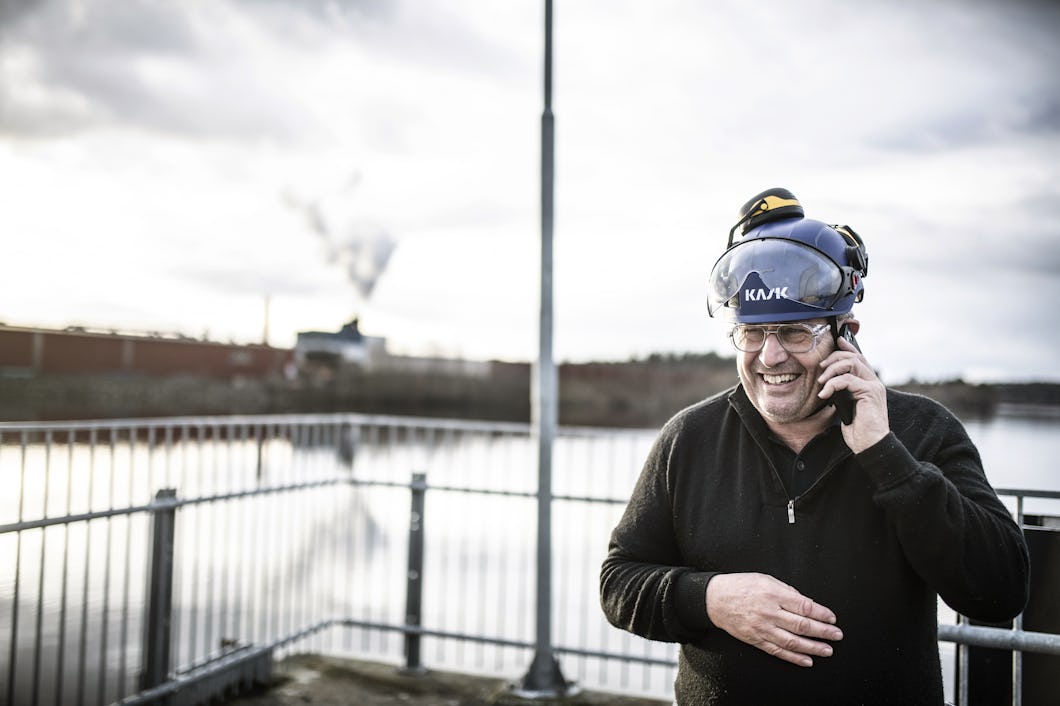 Sven Fahlén med hjälm pratar i telefon och står nära ett räcke med en industriell bakgrund.