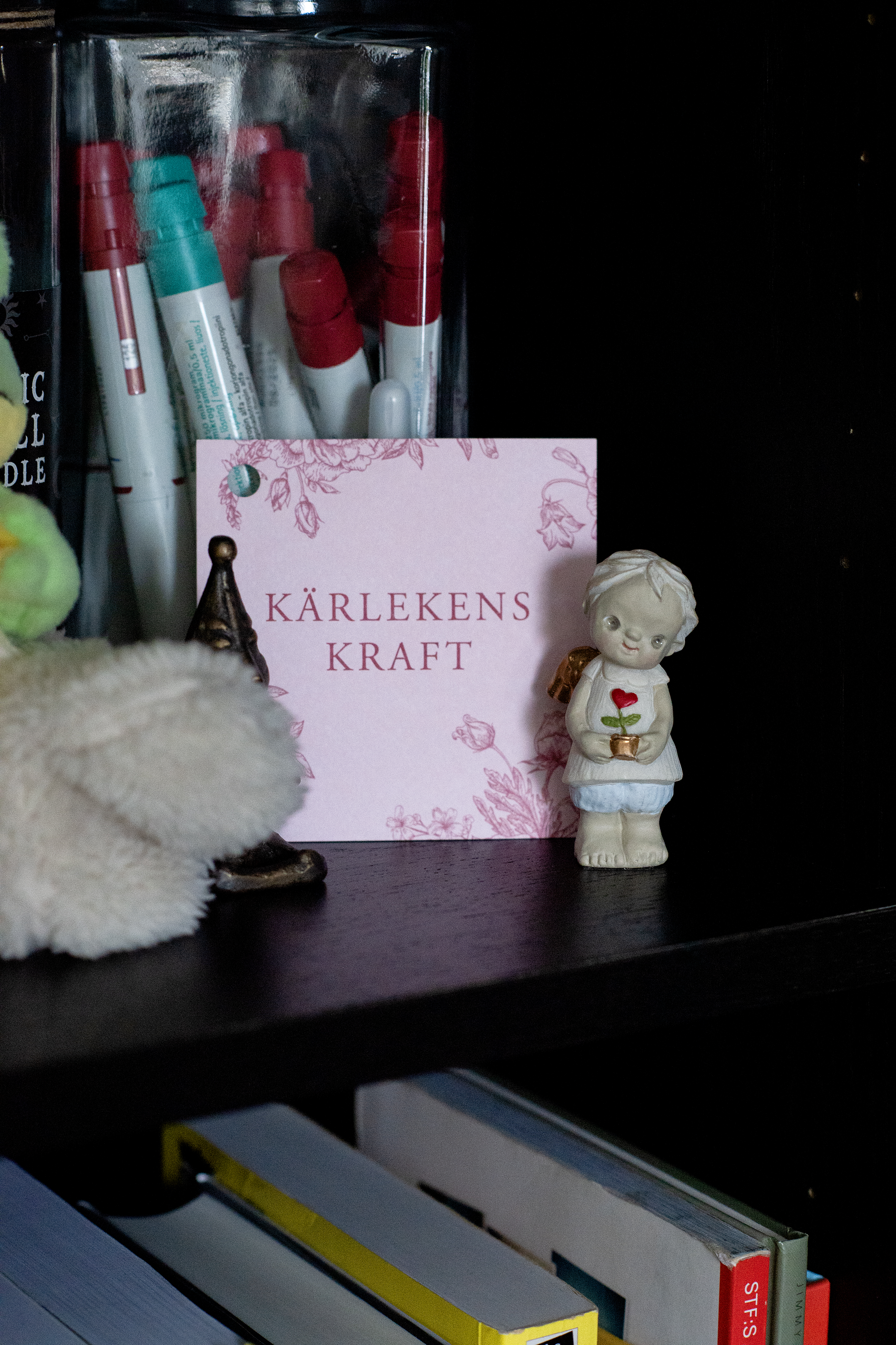 Hylla med pennor, ett kort märkt ”Kärlekens Kraft”, en liten figur som håller en ros och diverse böcker.