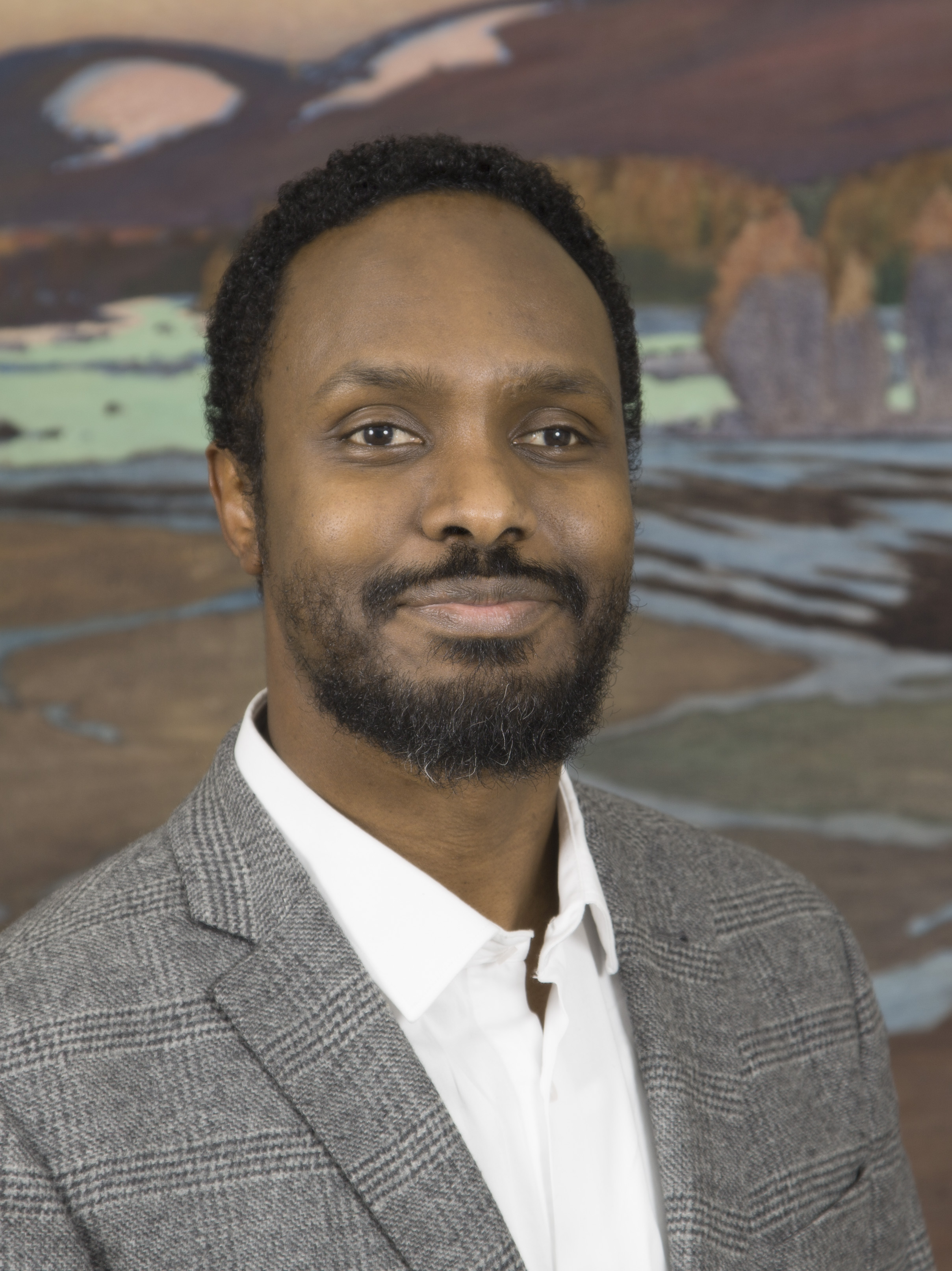 En man iklädd en grå kavaj och vit skjorta står framför en naturskön bakgrund.