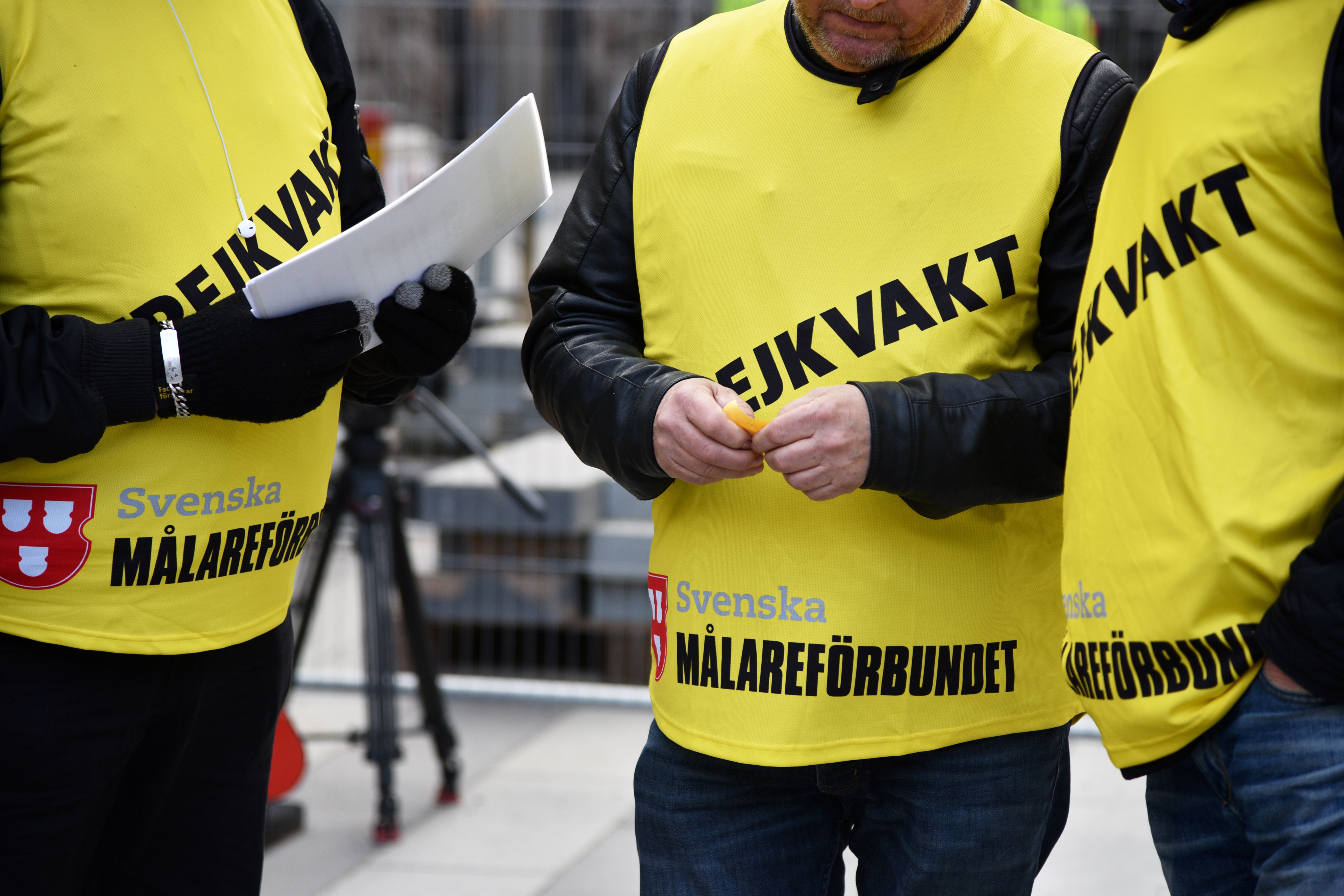 Tre personer i gula västar med texten "Svenska Målareförbundet" står tillsammans. En av dem håller i en surfplatta.