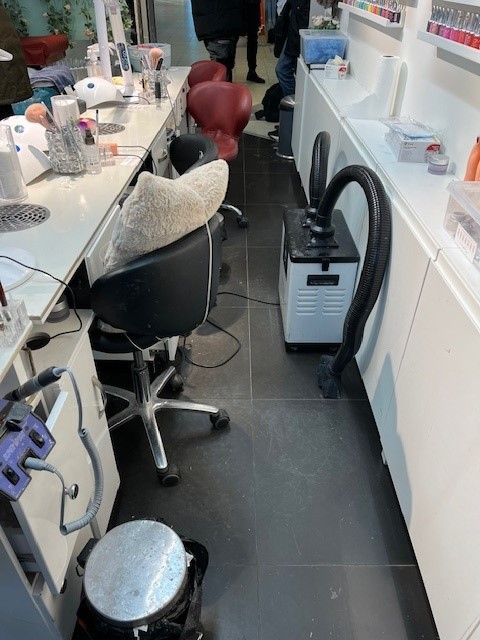 Bild på en nagelsalong med arbetsstationer som har stolar, en dammsugare på golvet och flaskor med nagellack på hyllor.