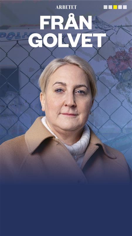 Person med kort hår som har på sig en ljusbrun kappa och vit polotröja, står framför ett stängsel med texten "FRÅN GOLVET" ovanför.