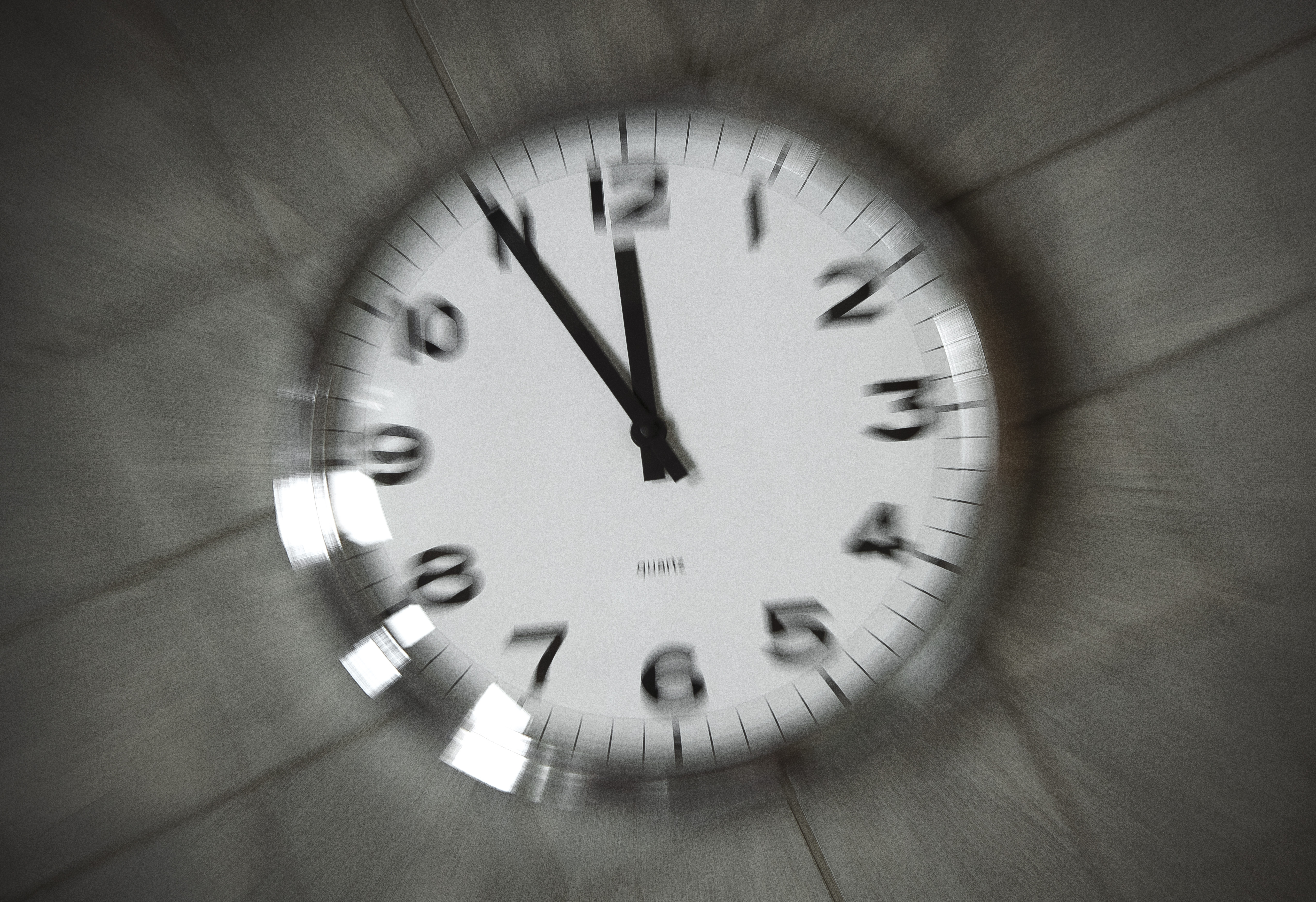 En suddig bild av en väggklocka som visar tid, med en ram av metall, mot en bakgrund av kakelvägg.