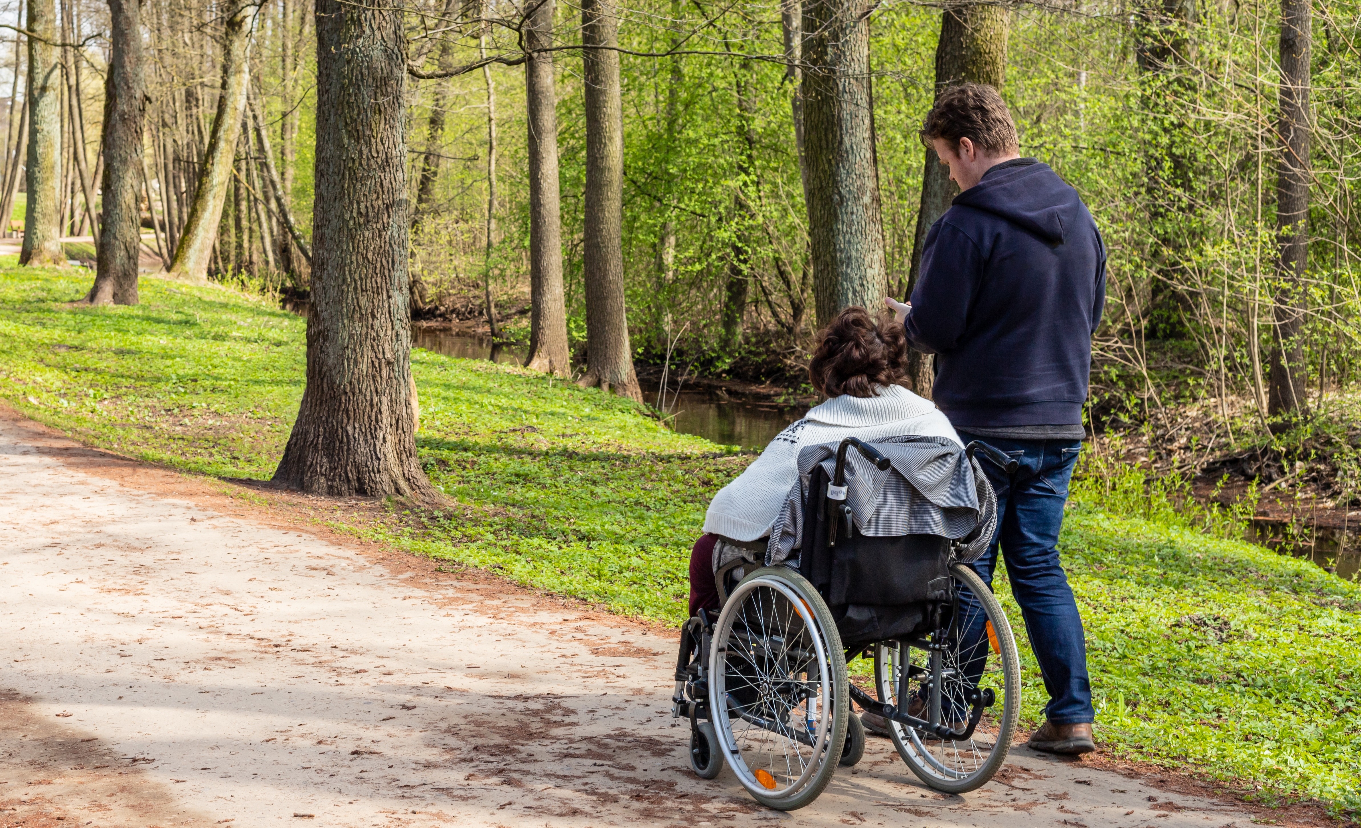 En person som skjuter en rullstolsburen individ längs en skogsstig.