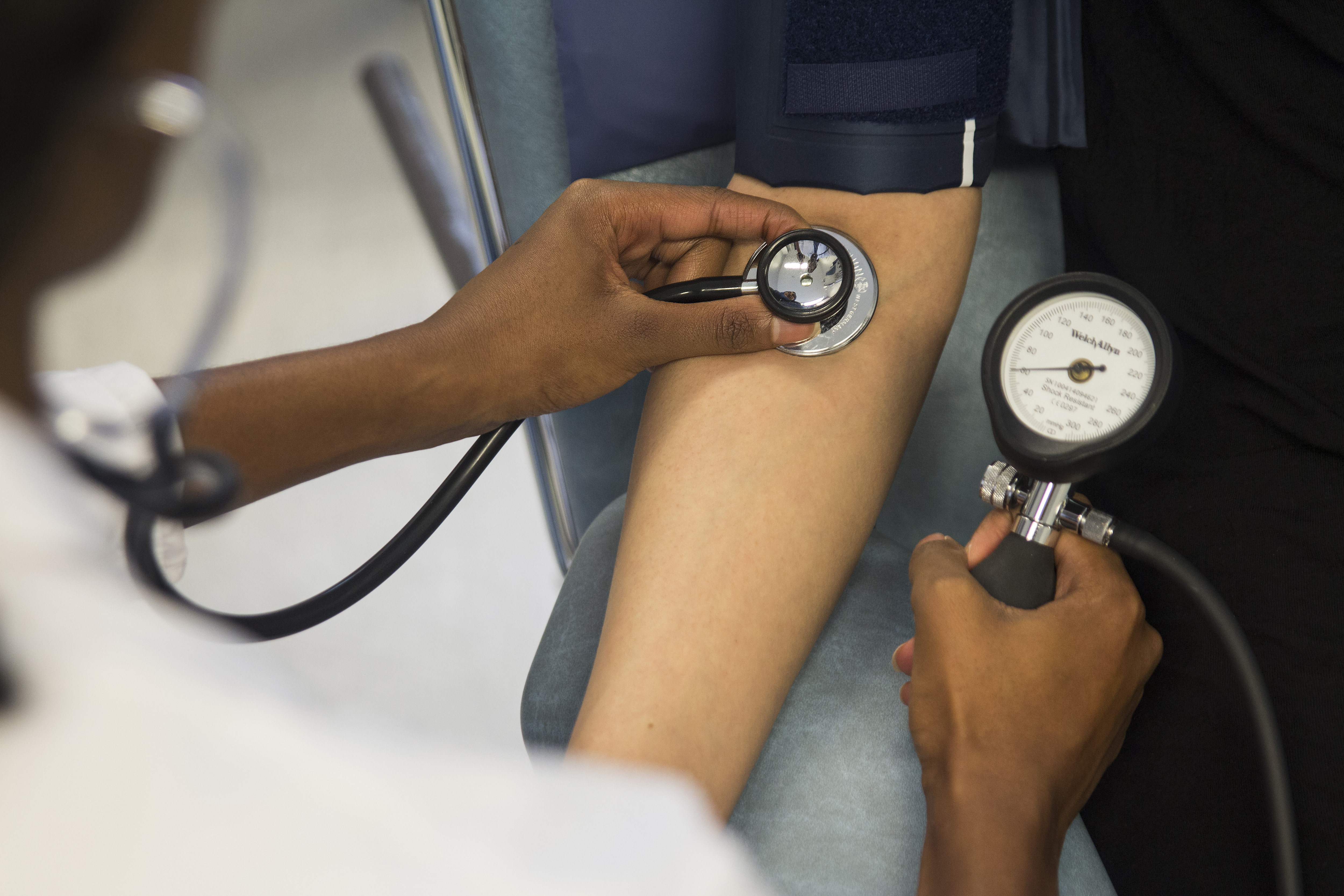En vårdpersonal kontrollerar en persons blodtryck med hjälp av en blodtrycksmätare och ett stetoskop.