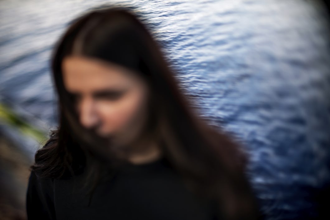 En person med långt mörkt hår står framför vatten.