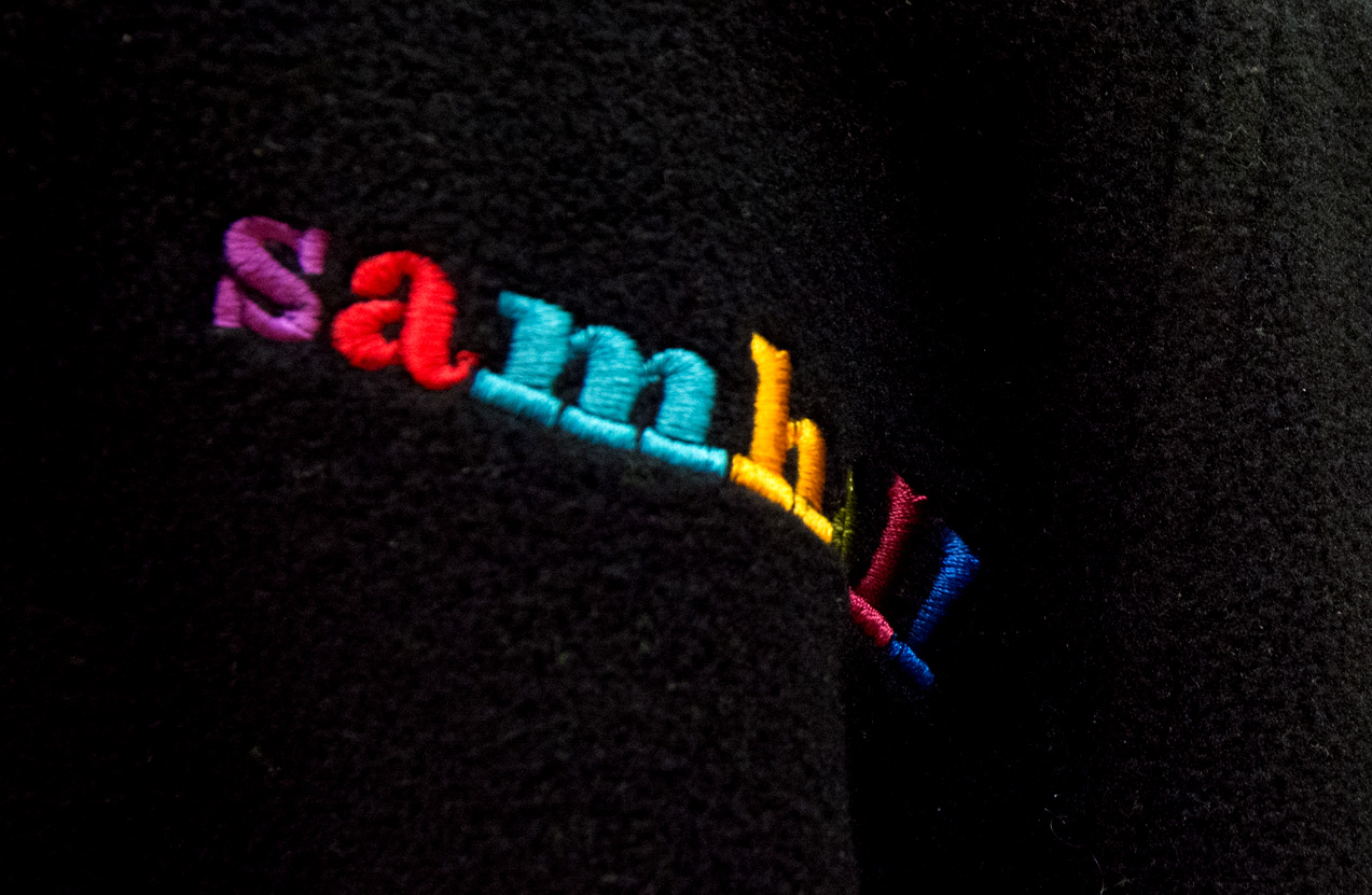 Närbild av broderade bokstäver på ett mörkt tyg som stavar "samball" med färgerna lila, röd, blå, gul och orange.