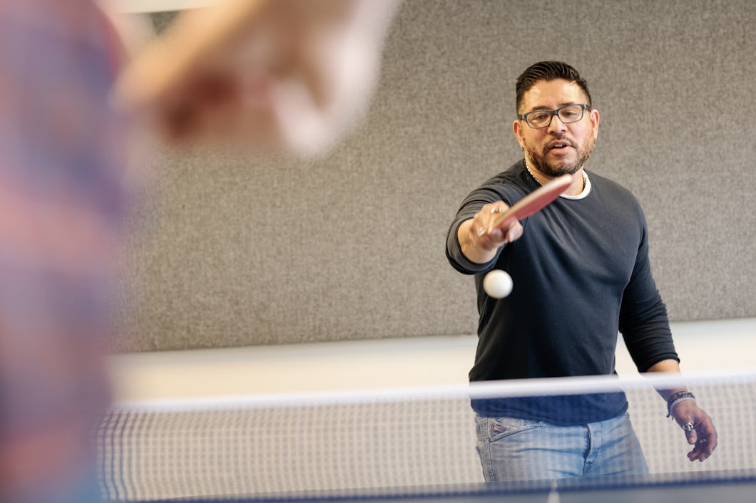 Magnus Hermansson spelar bordtennis och sträcker ut racketen för att slå bollen. En annan spelare syns delvis i förgrunden.
