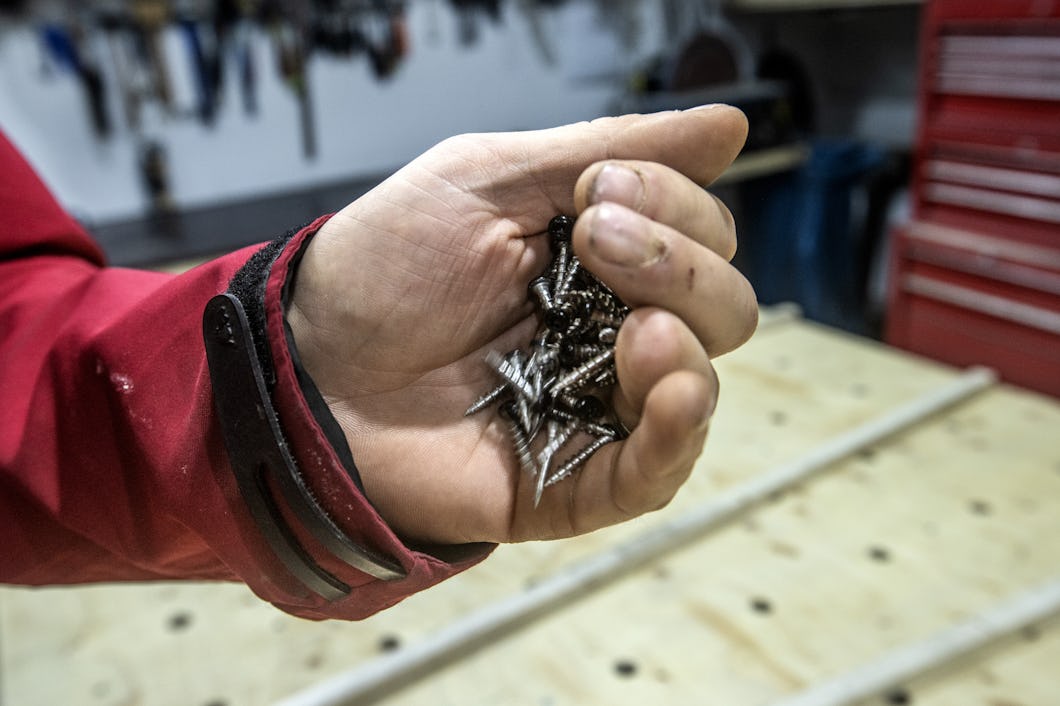 Matias Hultgren med ett rött plagg på armen håller en handfull metallskruvar i en verkstad.
