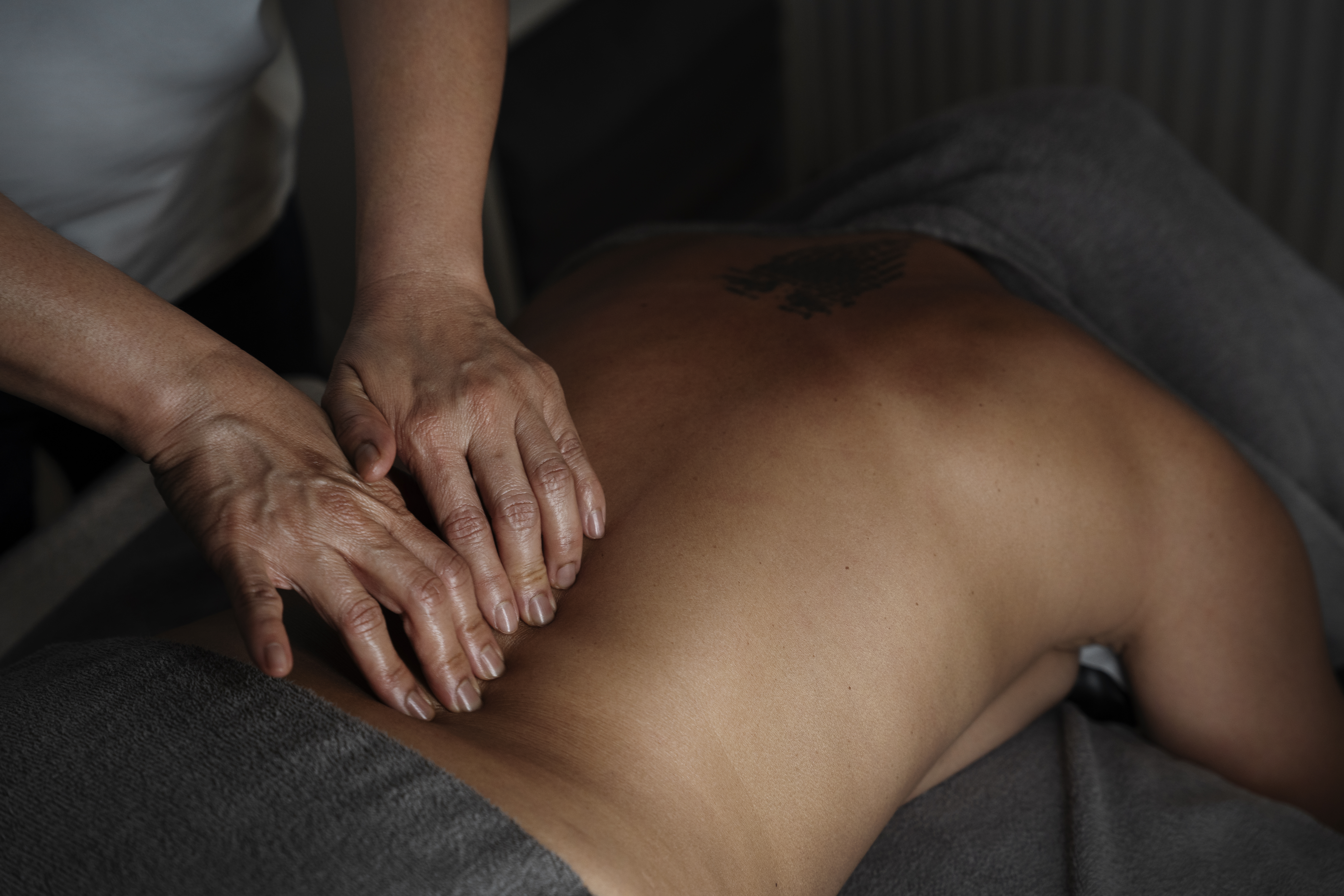 En person får massage på ryggen där händer trycker mot bar hud i svag belysning.