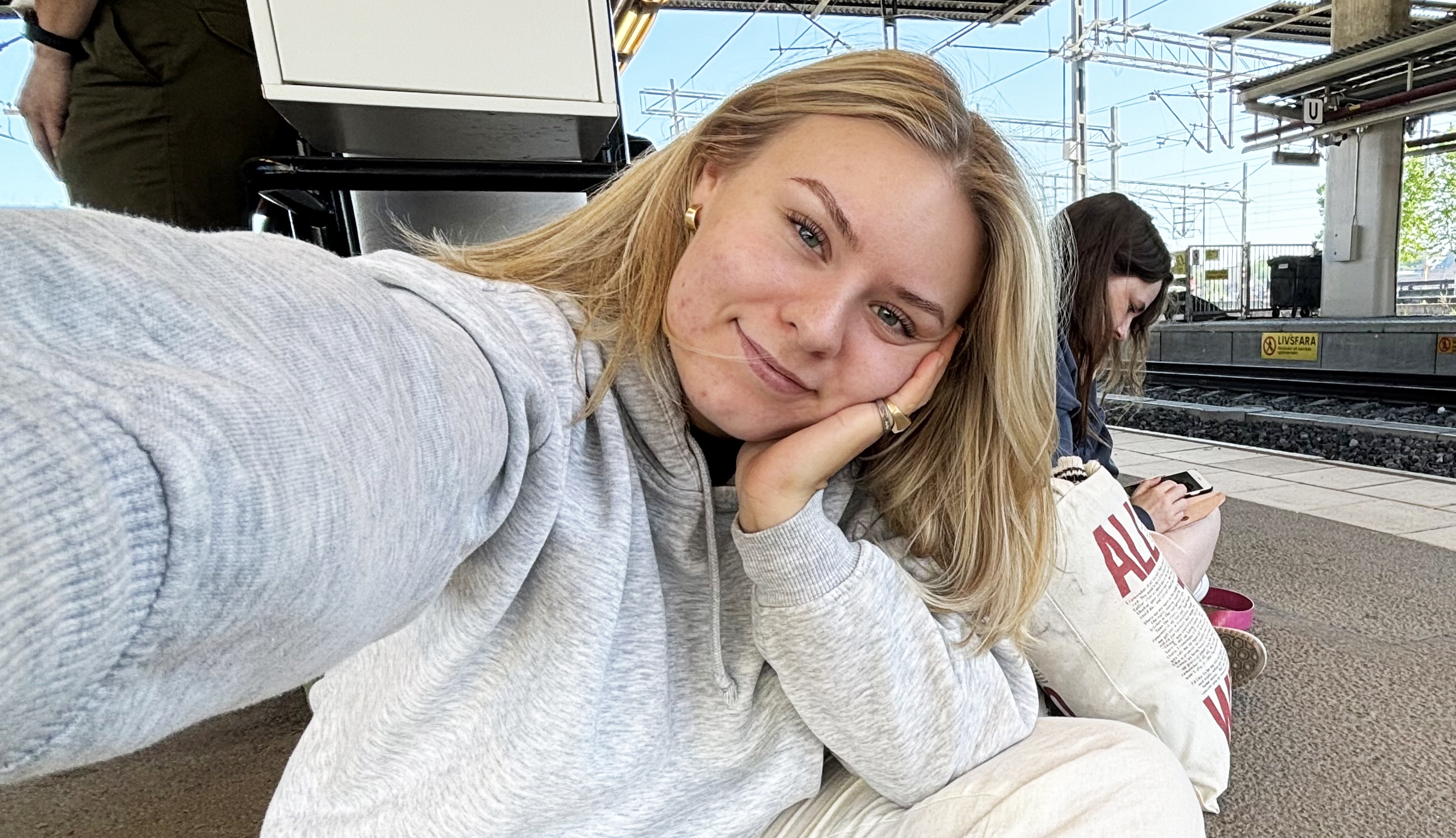 En person i grå tröja tar en selfie på en tågstation.