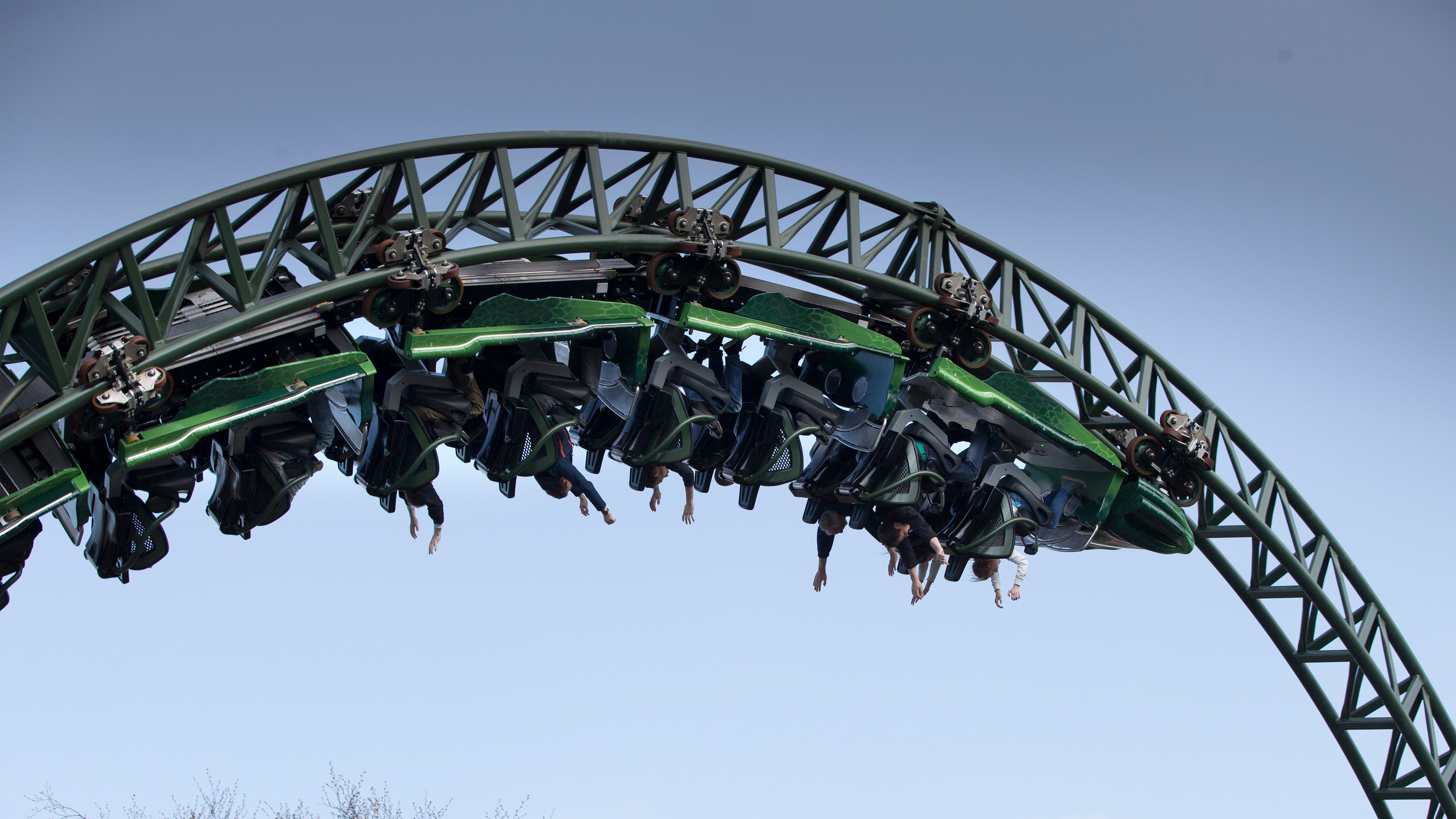 Personer åker en grön berg- och dalbana upp och ner i en loop mot en molnfri himmel.