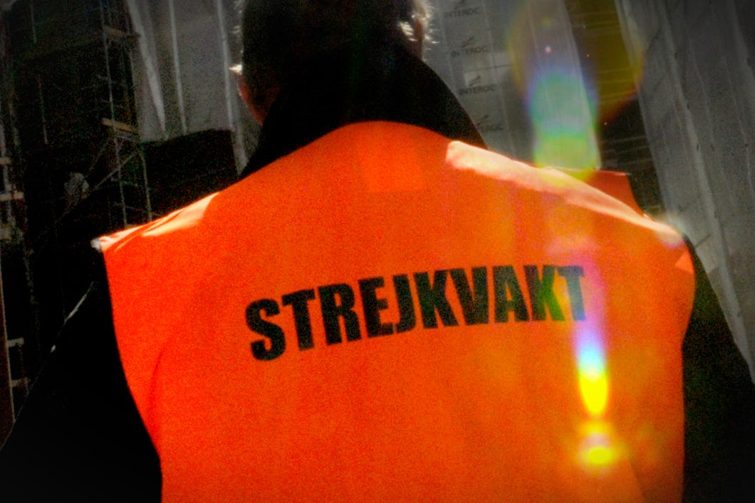 En person har på sig en orange väst med ordet ”Strejkvakt” tryckt på ryggen.