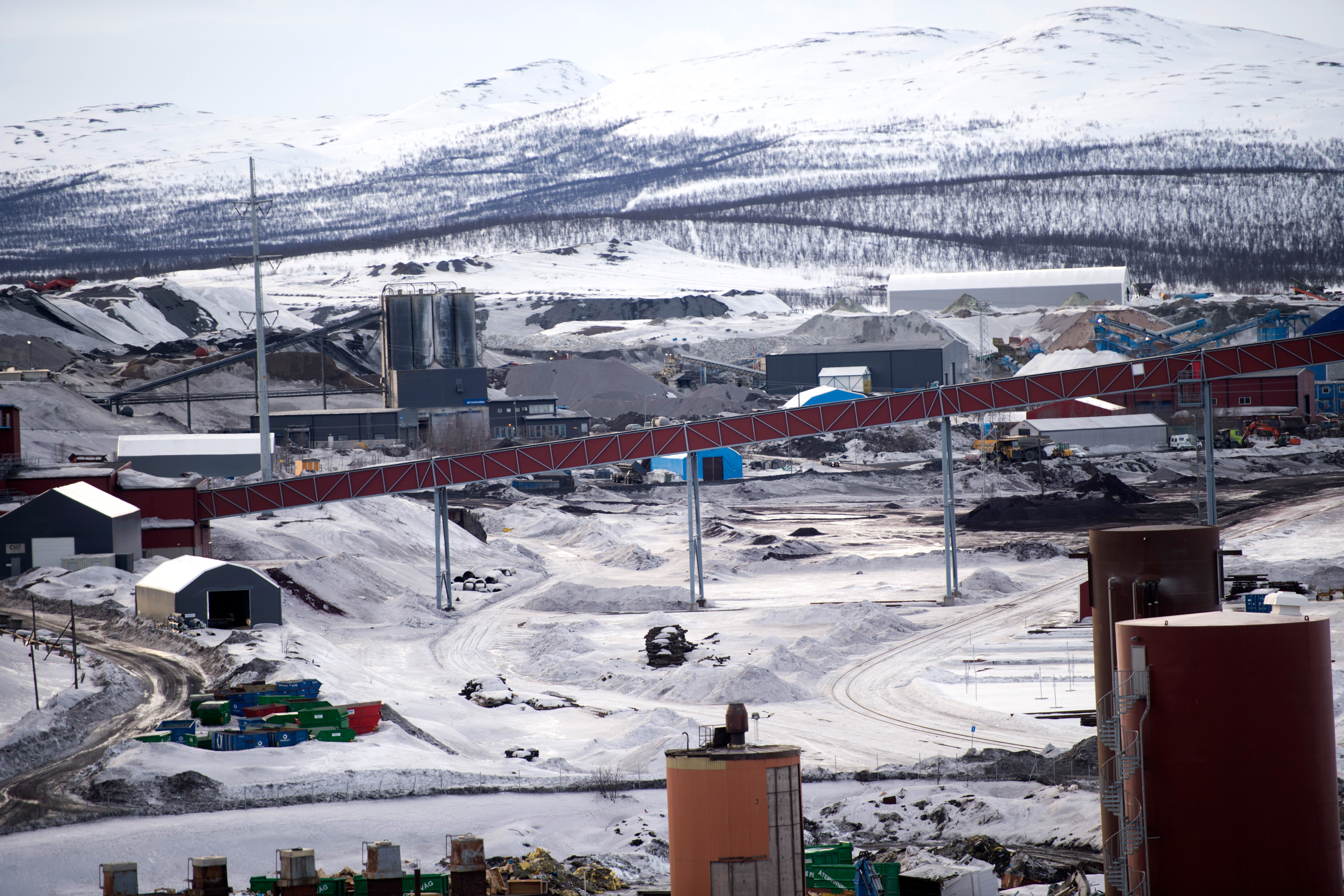 En industrigruva med transportband och maskiner ligger i ett snötäckt bergsområde.