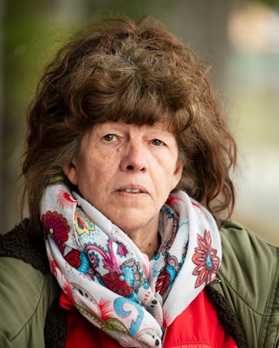 Saara Gustafsson med brunt hår och allvarsam uppsyn har på sig en grön jacka, en röd tröja med Kommunal-märke och en scarf med flera färger och står utomhus.