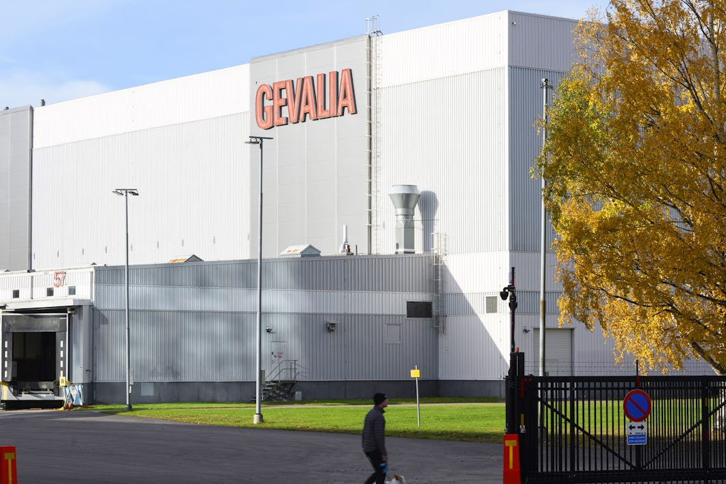 En industribyggnad med skylten "Gevalia" har lastkajer på ena sidan. Framför byggnaden går en person förbi ett svart stängsel.